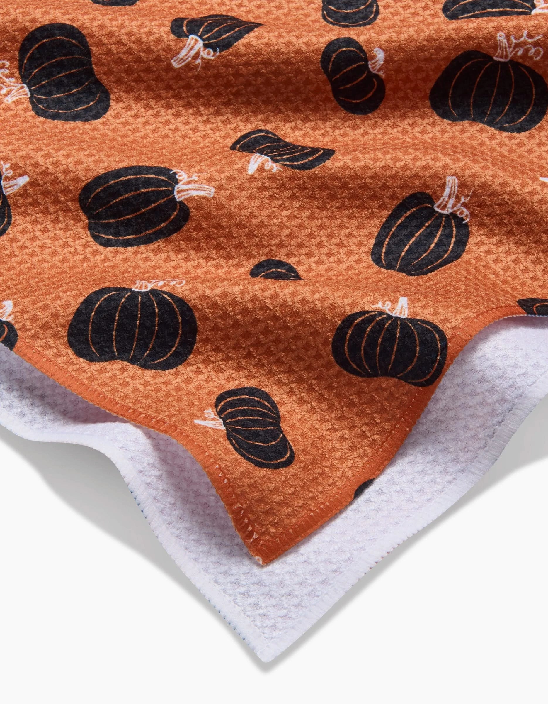A close-up of the Hufton Studio Halloween Black Pumpkins towel—an ultra-absorbent orange tea towel with black pumpkin prints, textured surface, and white reverse, perfect for adding festive flair to your kitchen.