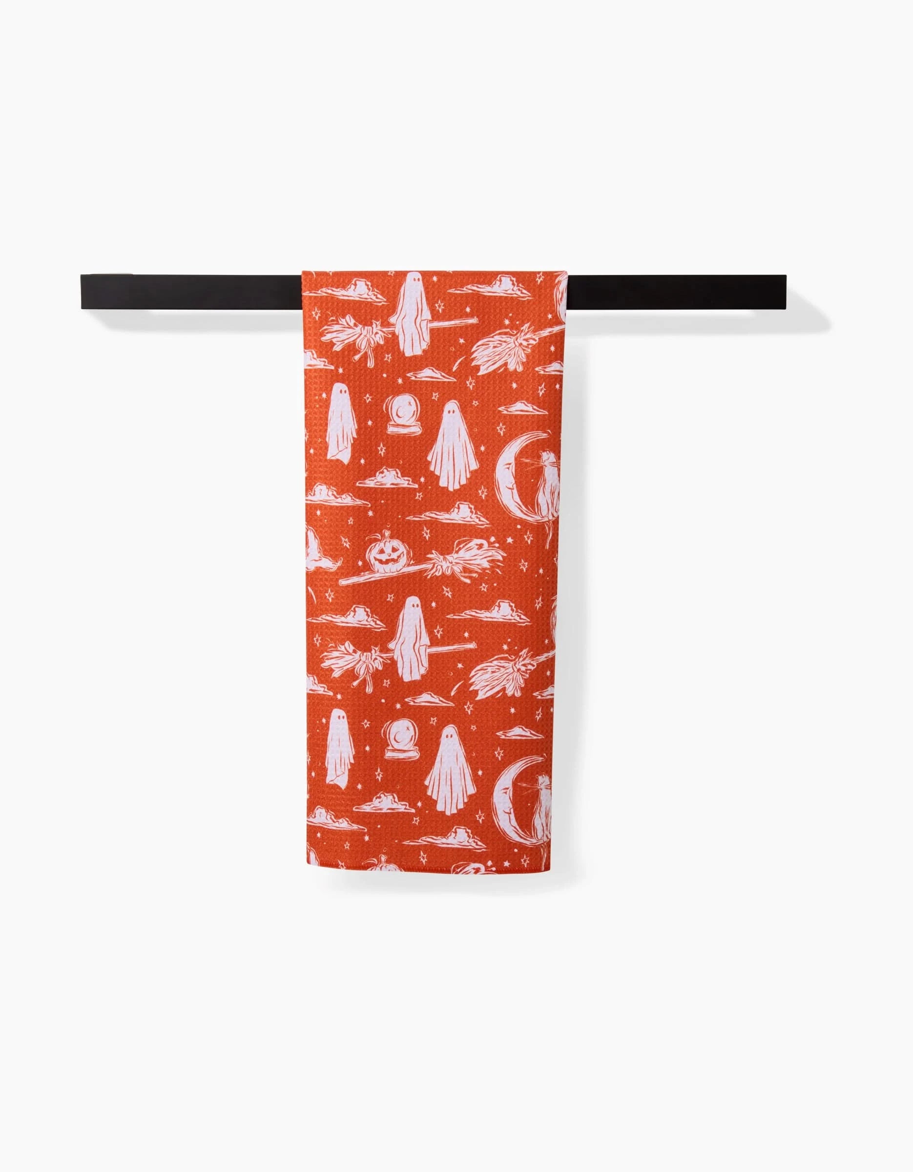 Aubrey Fairchild’s “Halloween Cats And Ghosts” recycled kitchen towel, featuring playful cats and ghosts, hangs neatly over a black bar against a plain white background.