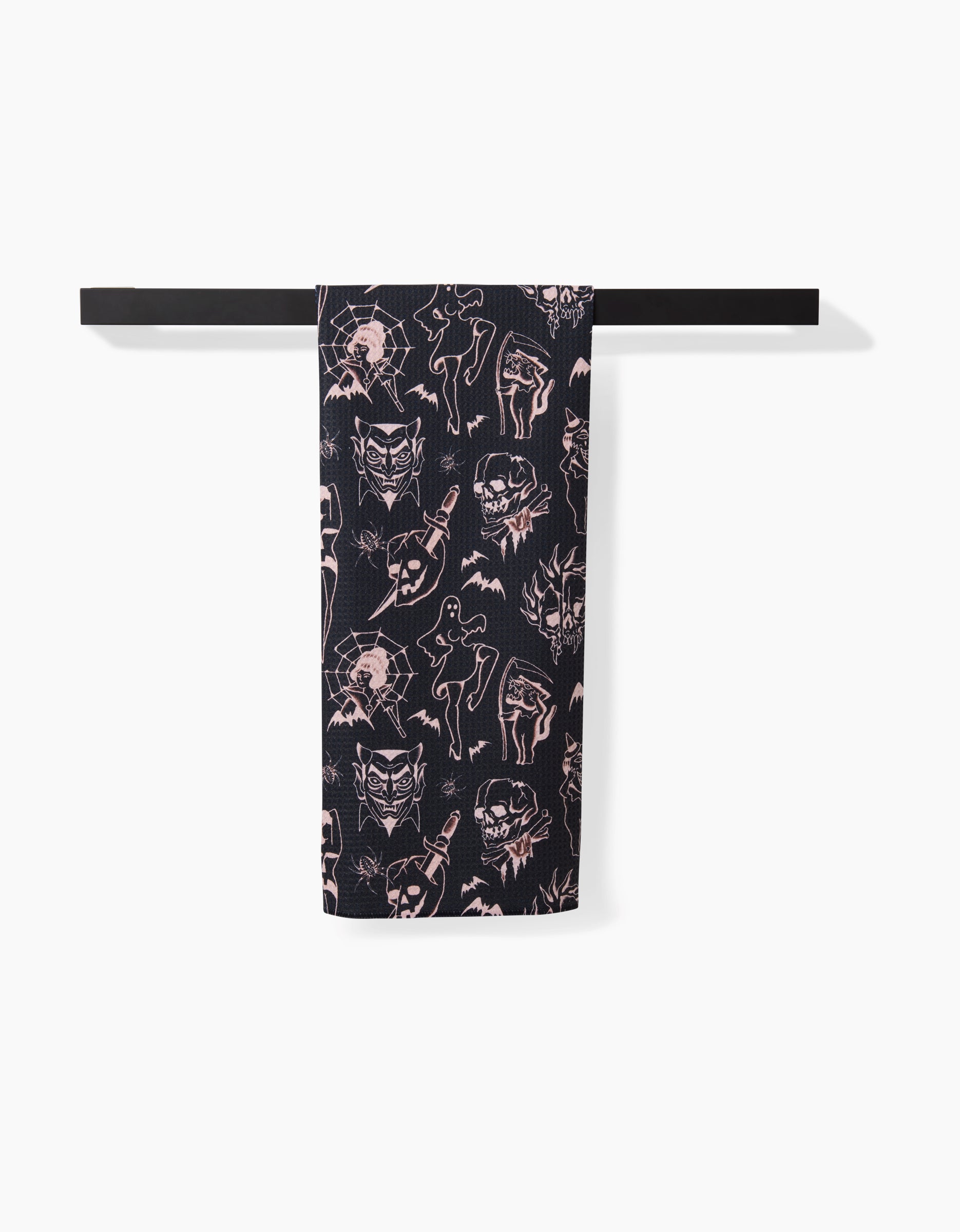 A black Halloween Flash tea towel by Cole Strem, with light pink tattoo-style skulls, spiders, bats, daggers, and mystical figures, hangs on a black bar. Made from premium Geoweave fabric for top absorbency and softness.