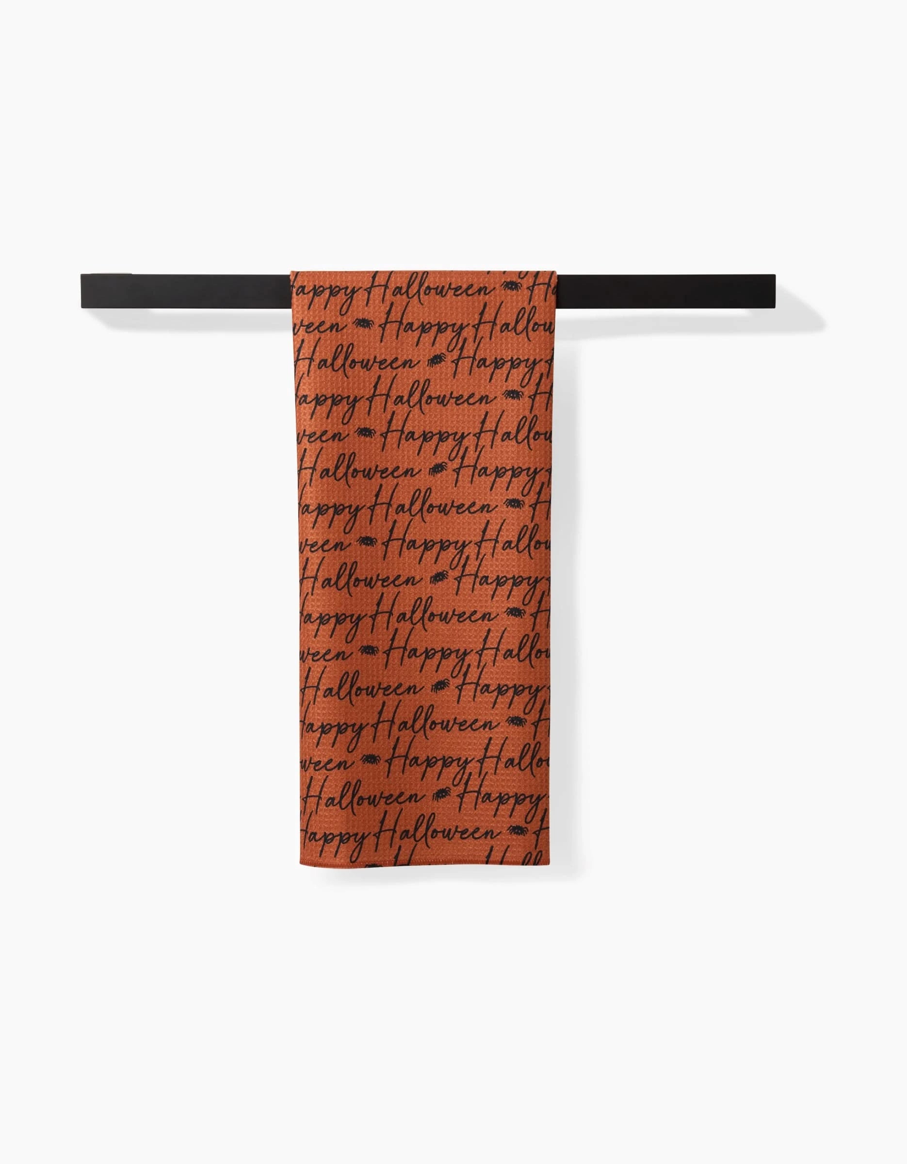 The Geometry Halloween Script Orange tea towel features a festive Happy Halloween black script on an orange background, hanging on a black bar. This ultra-absorbent towel brings seasonal charm and practicality to your kitchen.