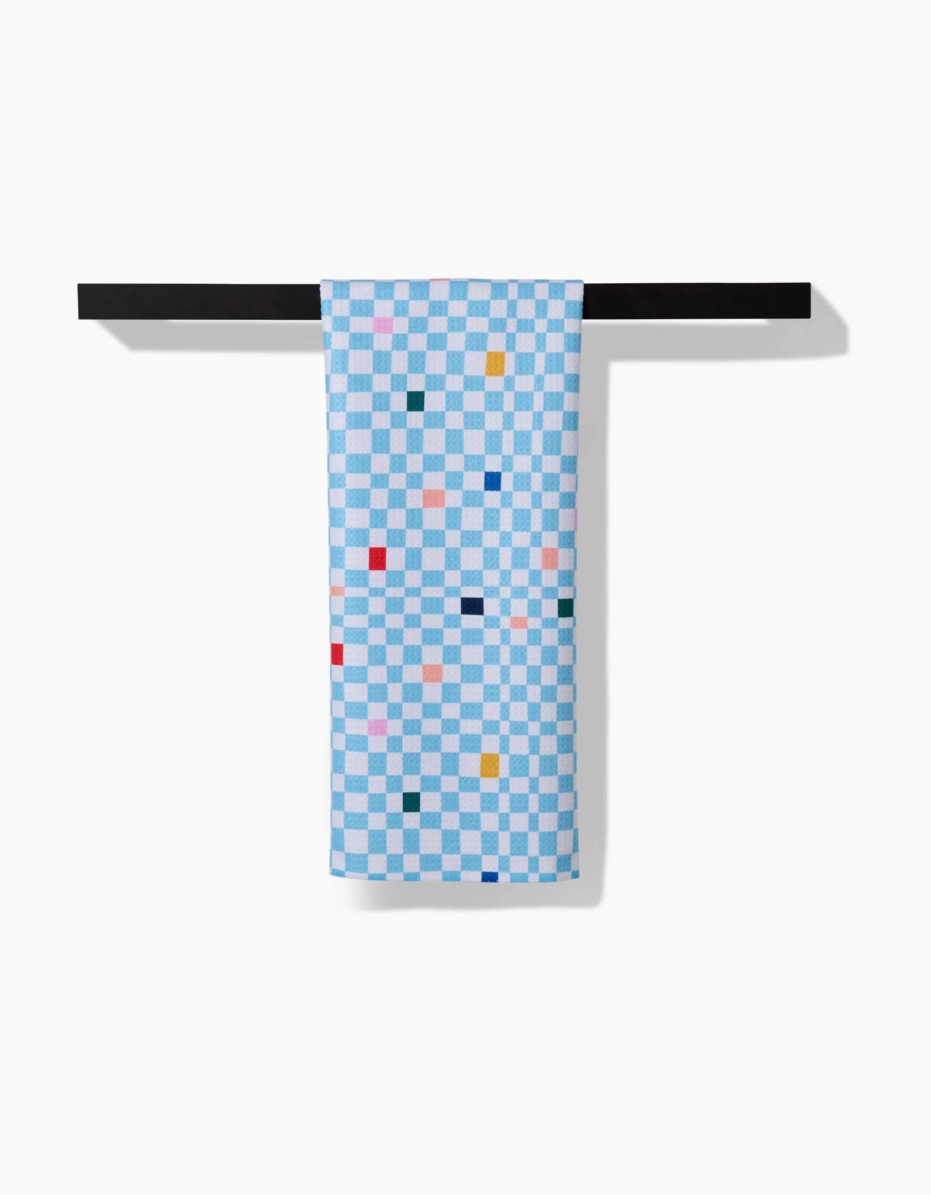 The Happy Hemera Happy Check tea towel, featuring a blue and white checkerboard with colorful squares, hangs neatly over a black bar, highlighting its ultra-absorbent Geoweave™ fabric against a white background.