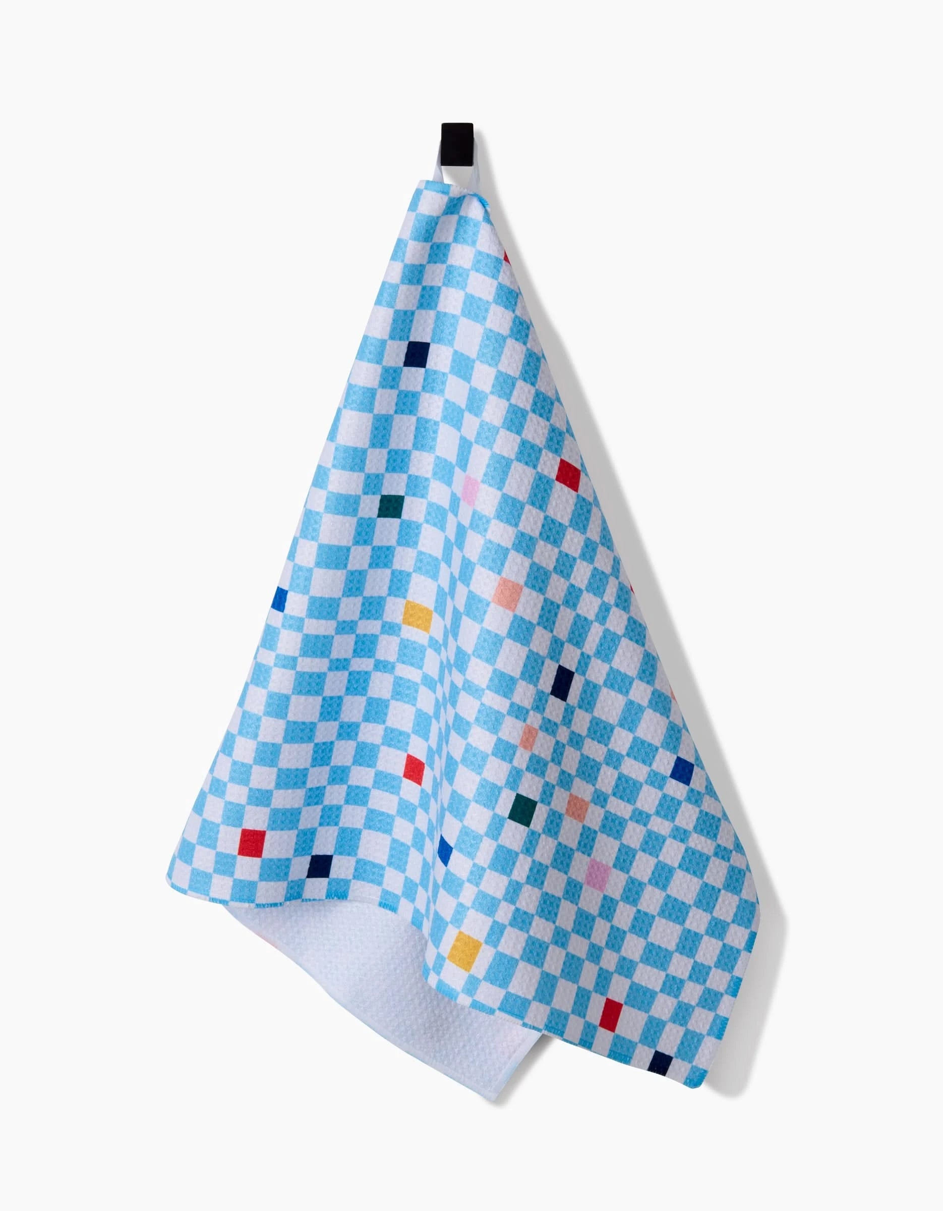 A Happy Hemera Happy Check tea towel, featuring blue and white checks with small colored squares and made from ultra-absorbent Geoweave™ fabric, hangs from a black hook against a plain white background.