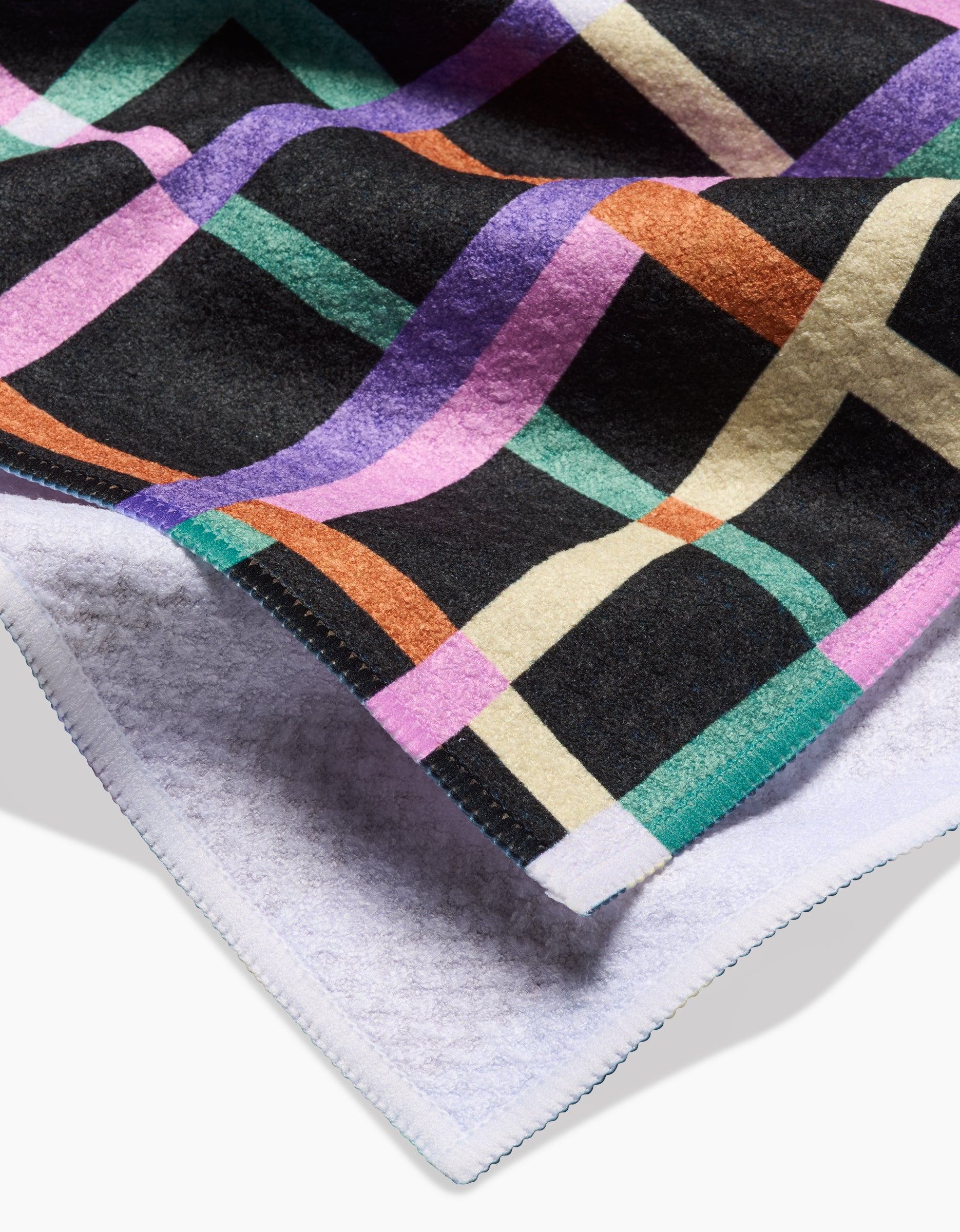 A close-up of Claire Iglesias Happy Plaid, featuring a colorful purple, green, orange, and cream pattern on black, crafted from soft Geoweave™ fabric with a white underside and neatly stitched edges.