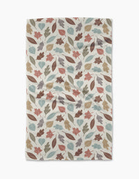 The Harvest Scatter tea towel by Sarah Daugherty features autumn leaves in brown, orange, teal, and beige on cream. Made from recycled materials, its slightly wrinkled finish gives a cozy, lived-in look.