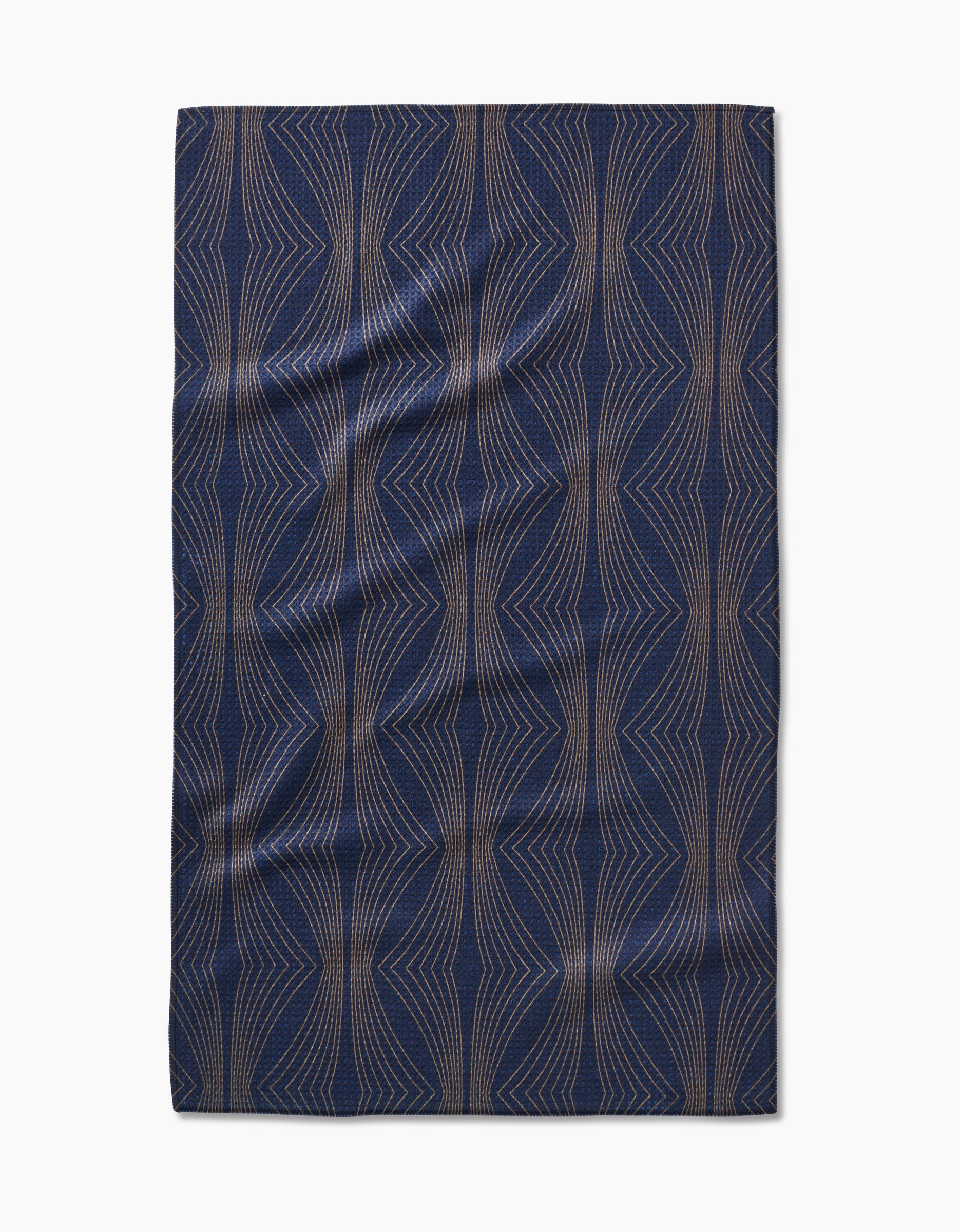 The Hera Tea Towel by Amy MacCready features navy blue Geoweave™ fabric with a geometric pattern of tan, symmetrical, wavy lines. The slightly wrinkled towel is shown flat on a white background.