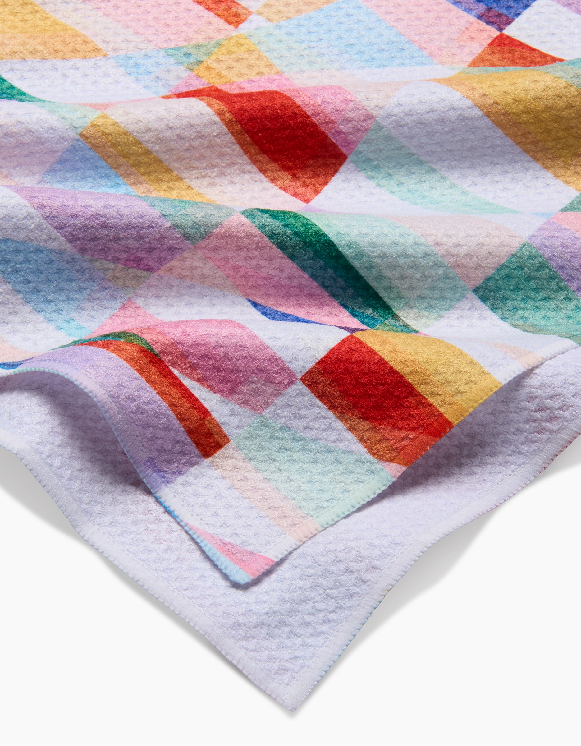 A soft, textured RACHEL PARKER Highlands Tea Towel with a colorful checkered pattern in red, yellow, green, blue, and pink. Partially folded to showcase its waffle-like Geoweave fabric.