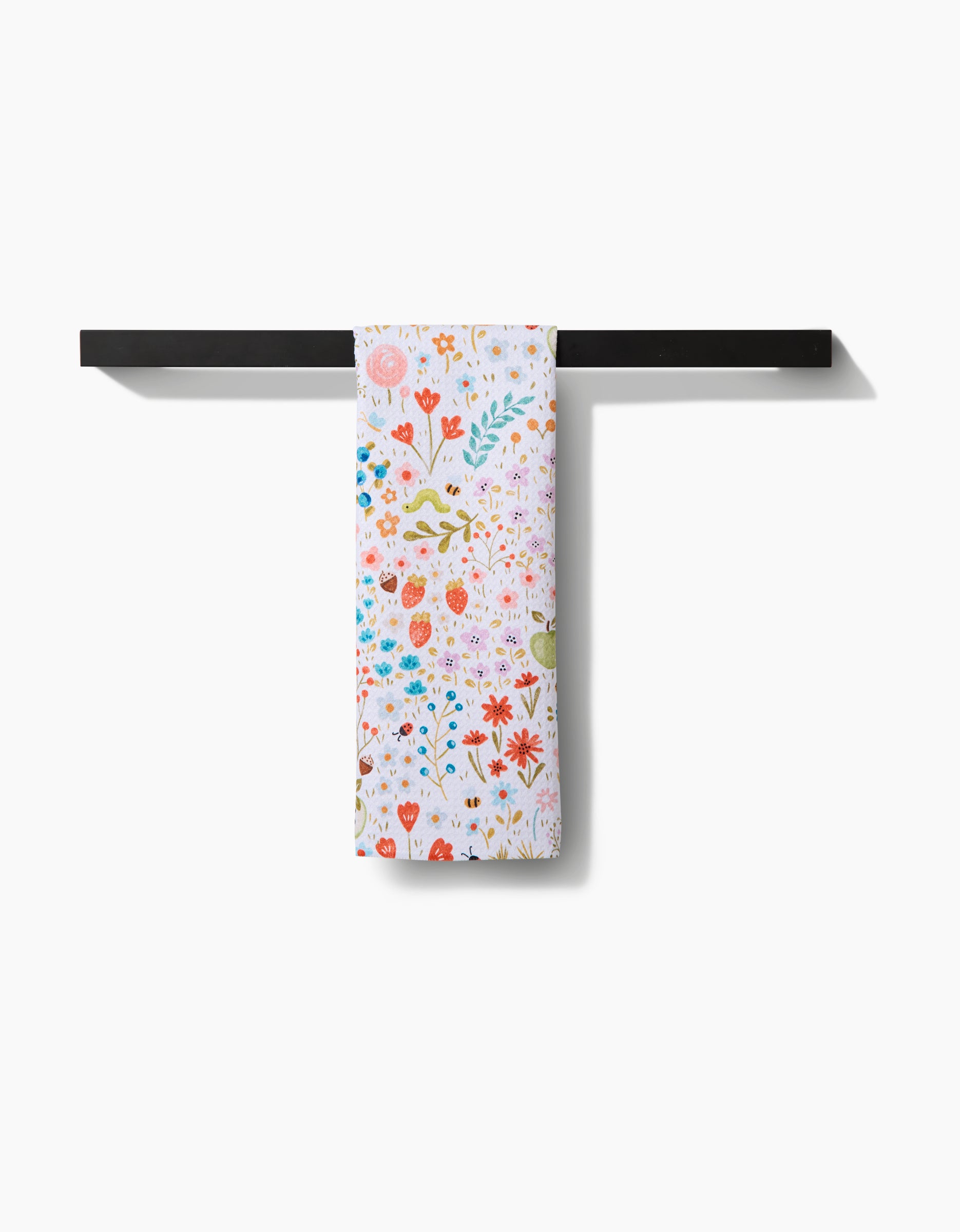 The Honeybee Heaven tea towel by Sara Mari, made from eco-friendly Geoweave fabric, features a colorful floral design and hangs neatly over a black bar on a white background.
