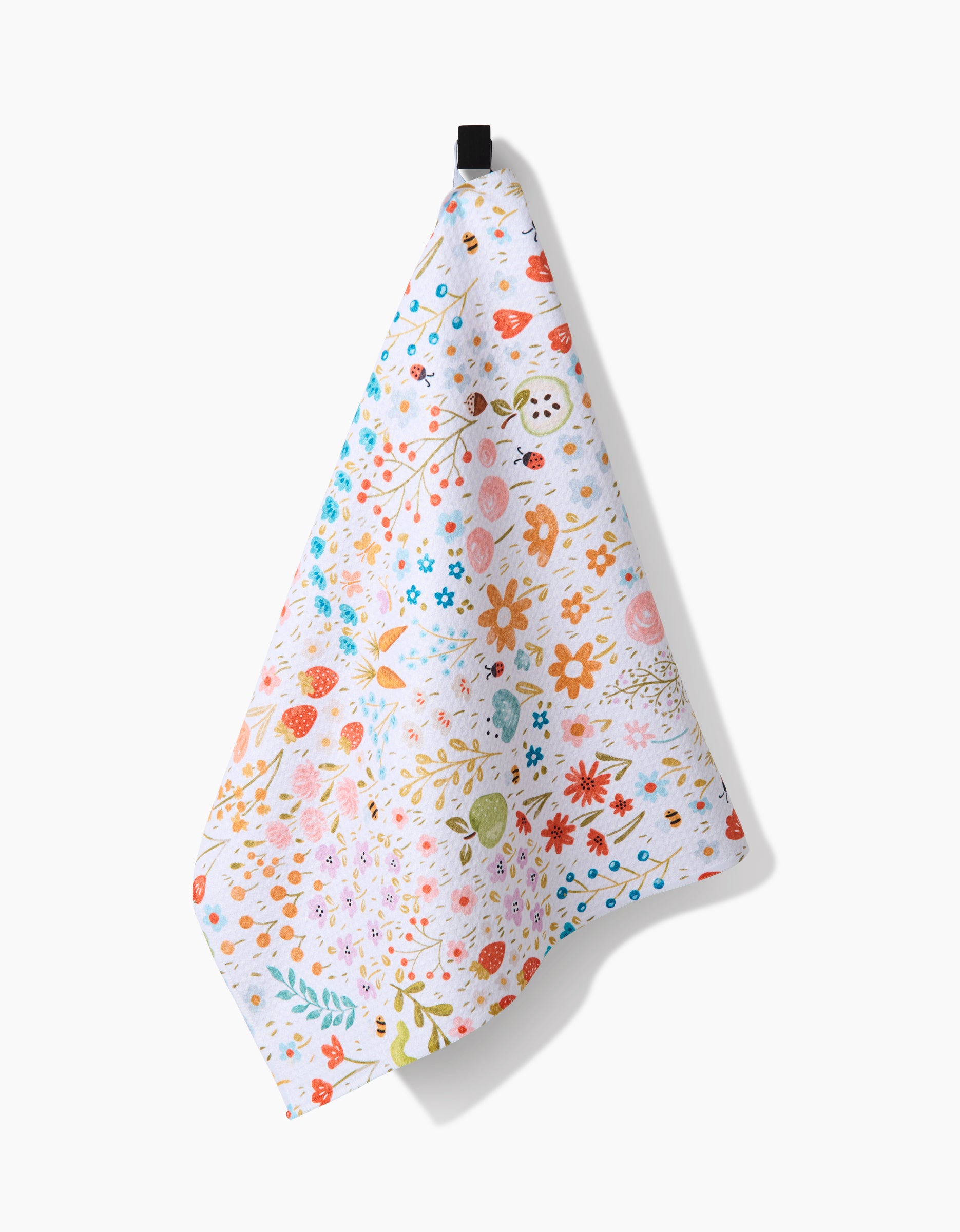 The Sara Mari Honeybee Heaven tea towel, crafted from eco-friendly Geoweave fabric, displays a bright floral pattern with red, orange, pink, green, and blue flowers and leaves. It hangs from a black loop against a white background.