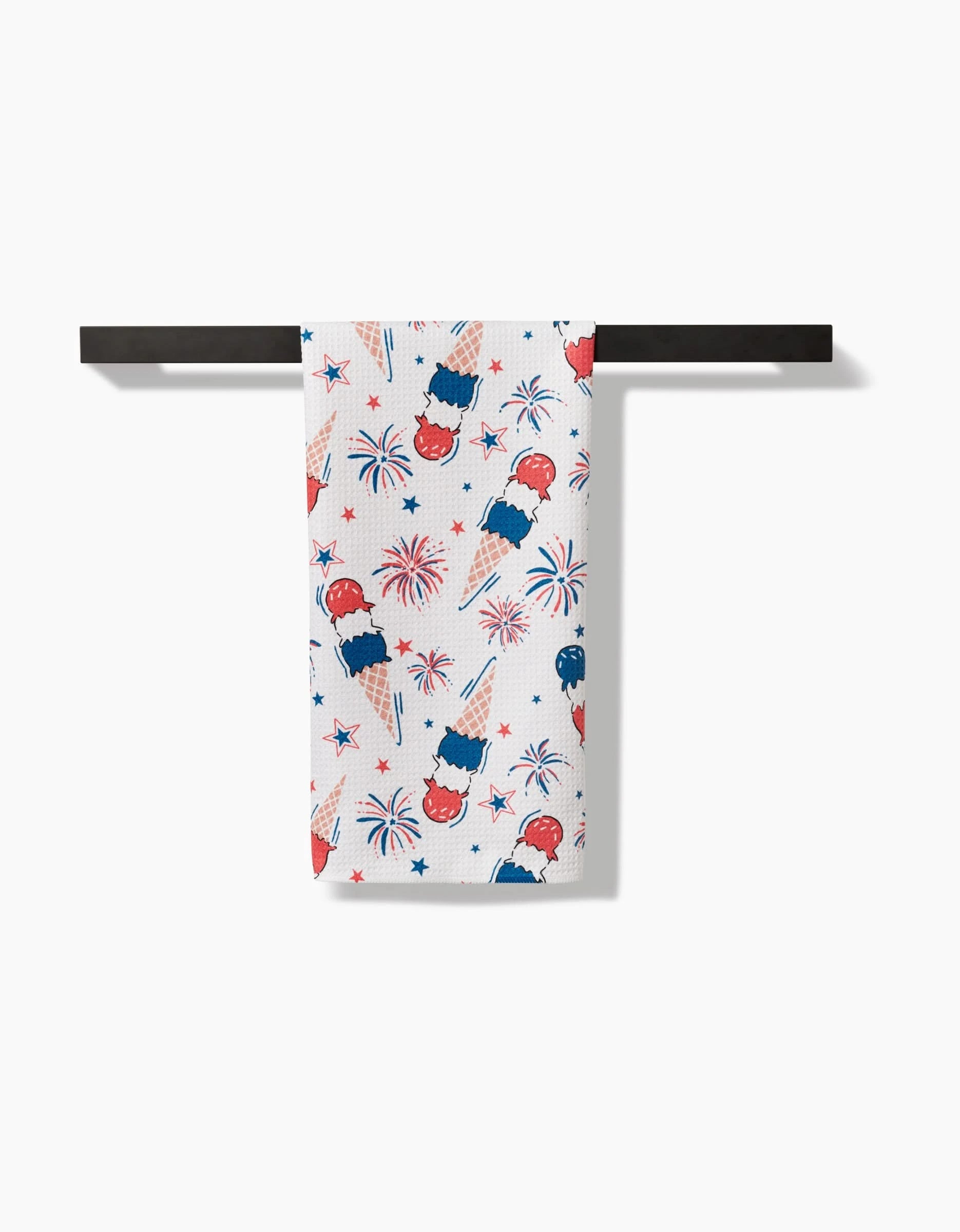 The Ice Cream Celebration tea towel by Hufton Studio features festive red, white, and blue popsicles, fireworks, and stars. Made from ultra-absorbent recycled materials, it adds charm when displayed on a black rod against a white background.