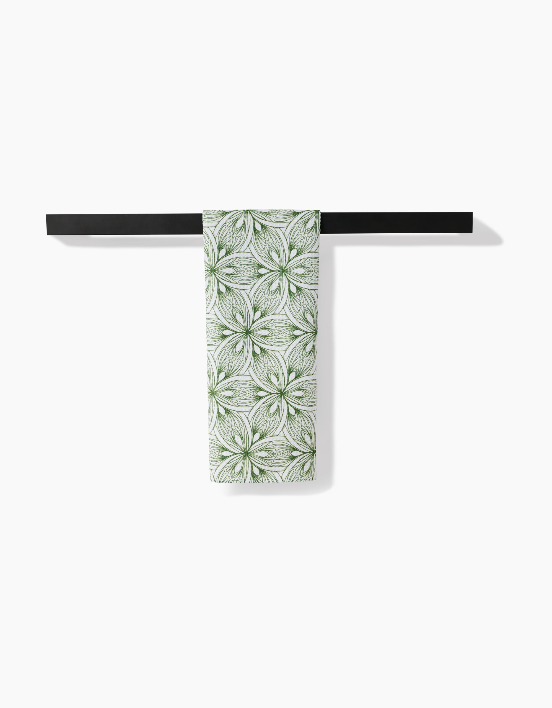 The Interlaced Petals tea towel by Marta Harvey, made from ultra-absorbent recycled materials with green and white floral patterns, hangs neatly over a simple black towel bar against a plain white background.