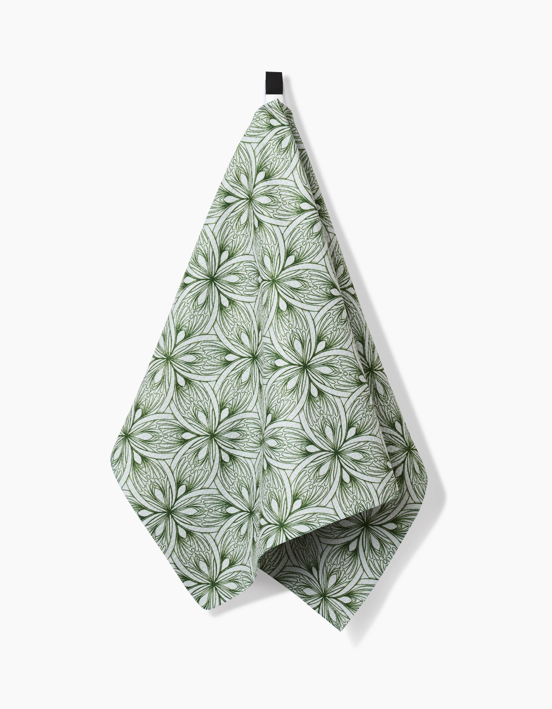 The Interlaced Petals tea towel by Marta Harvey, crafted from recycled materials, showcases a green and white floral pattern of overlapping petals and hangs by a black loop against a plain white background.