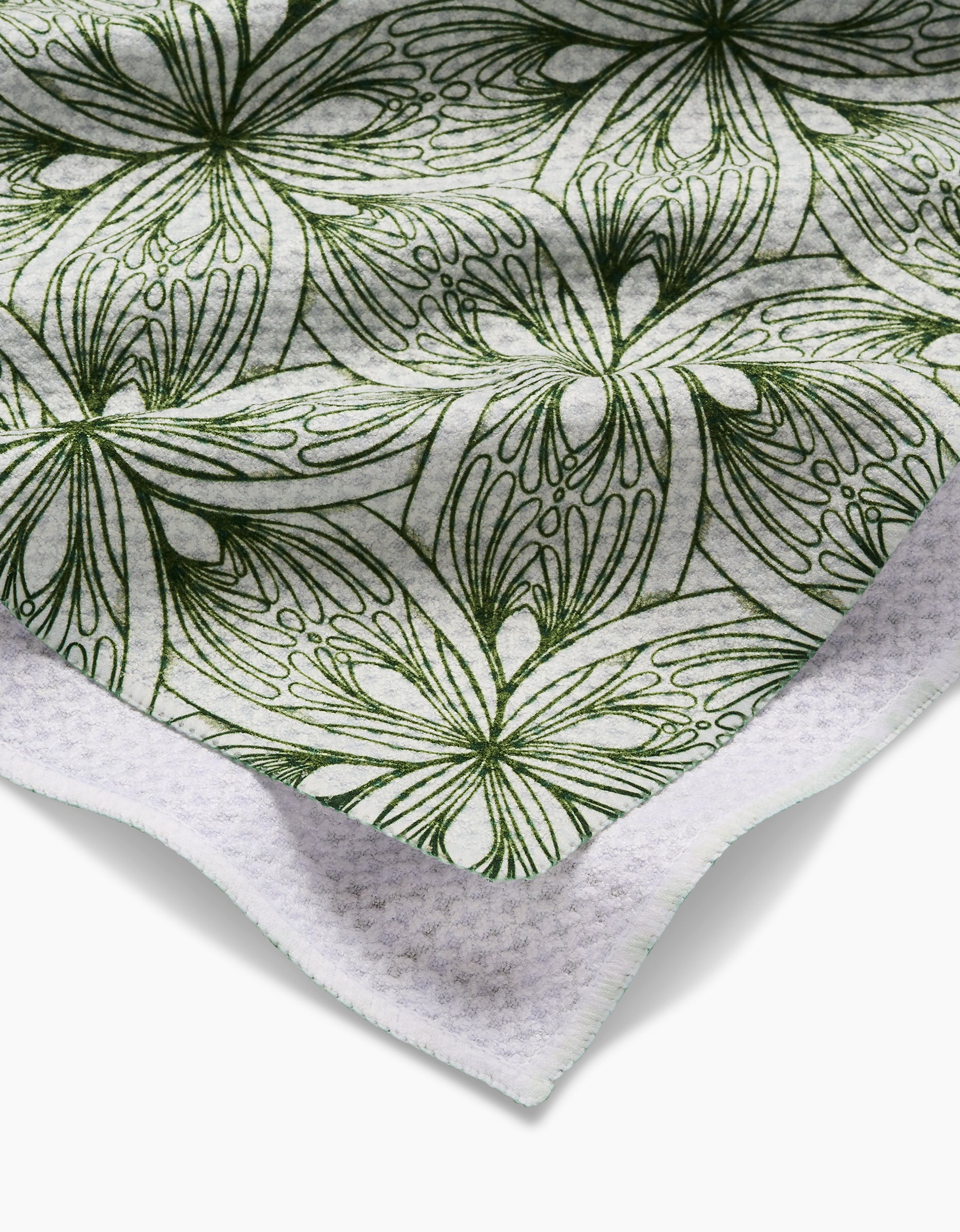 A close-up of the Marta Harvey Interlaced Petals tea towel shows its green abstract floral pattern on white, with textured edges and an ultra-absorbent, waffle-like underside made from recycled materials.