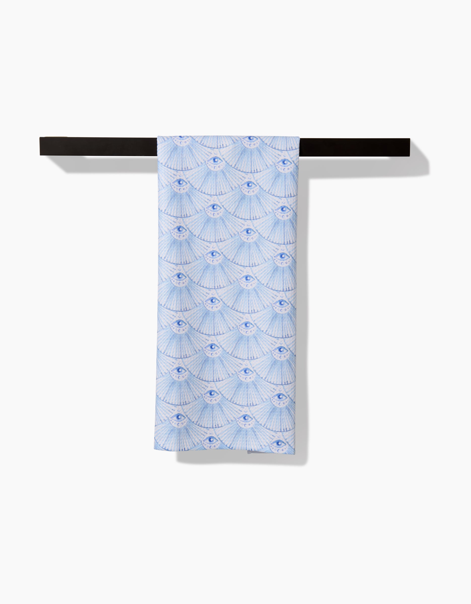 The Into The Mystic tea towel by Maayan Alper-Swan, crafted with absorbent Geoweave fabric, showcases a blue and white shell-inspired pattern and hangs neatly over a black bar against a plain white background.