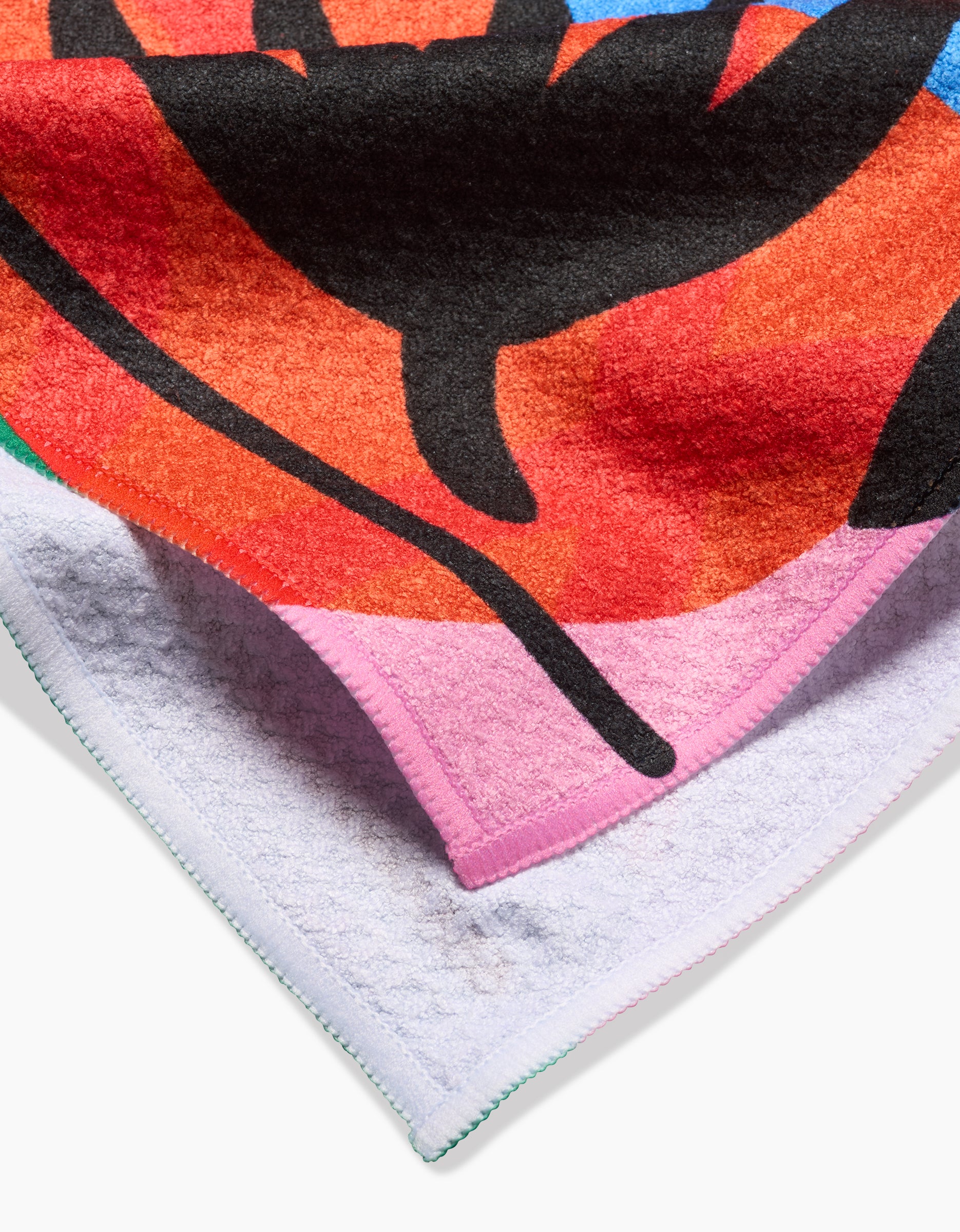 A close-up of Jacaré by Camila Leão: a bold, abstract tea towel with black, red, pink, and orange on the front and plain light purple recycled Geoweave fabric on the reverse.