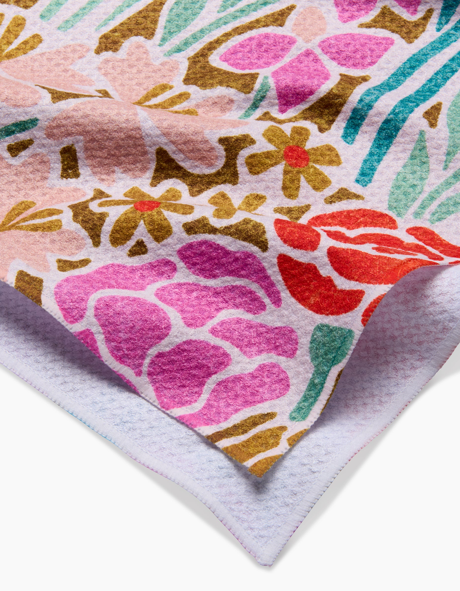 A close-up of the Janae tea towel by Amy MacCready, featuring a soft Geoweave fabric with a colorful floral pattern—pink, red, yellow, and green on white. A corner is folded to reveal the plain white underside.