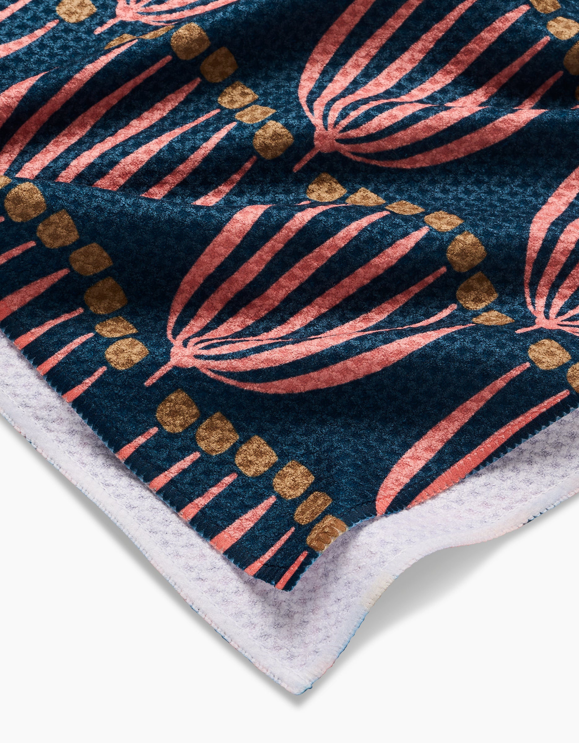 A close-up of the Josie Tea Towel by Amy MacCready, featuring ultra-absorbent Geoweave™ fabric with a colorful pink leaf and gold dot pattern on dark blue and a white-edged border.