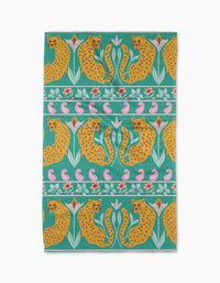 The Jungle Blooms tea towel by Jasmine Blooms Designs features yellow cheetahs, pink flowers, and green leaves in a repeating pattern on a teal background with horizontal stripes.