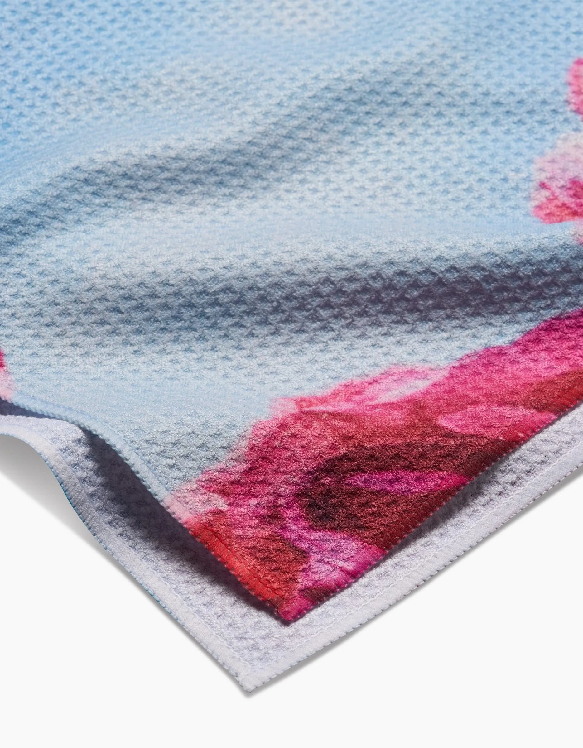 A close-up of the Stefanie Bales La Floraison Geoweave™ Tea Towel, light blue with a waffle texture, pink and red floral edge designs, and crafted from recycled materials.