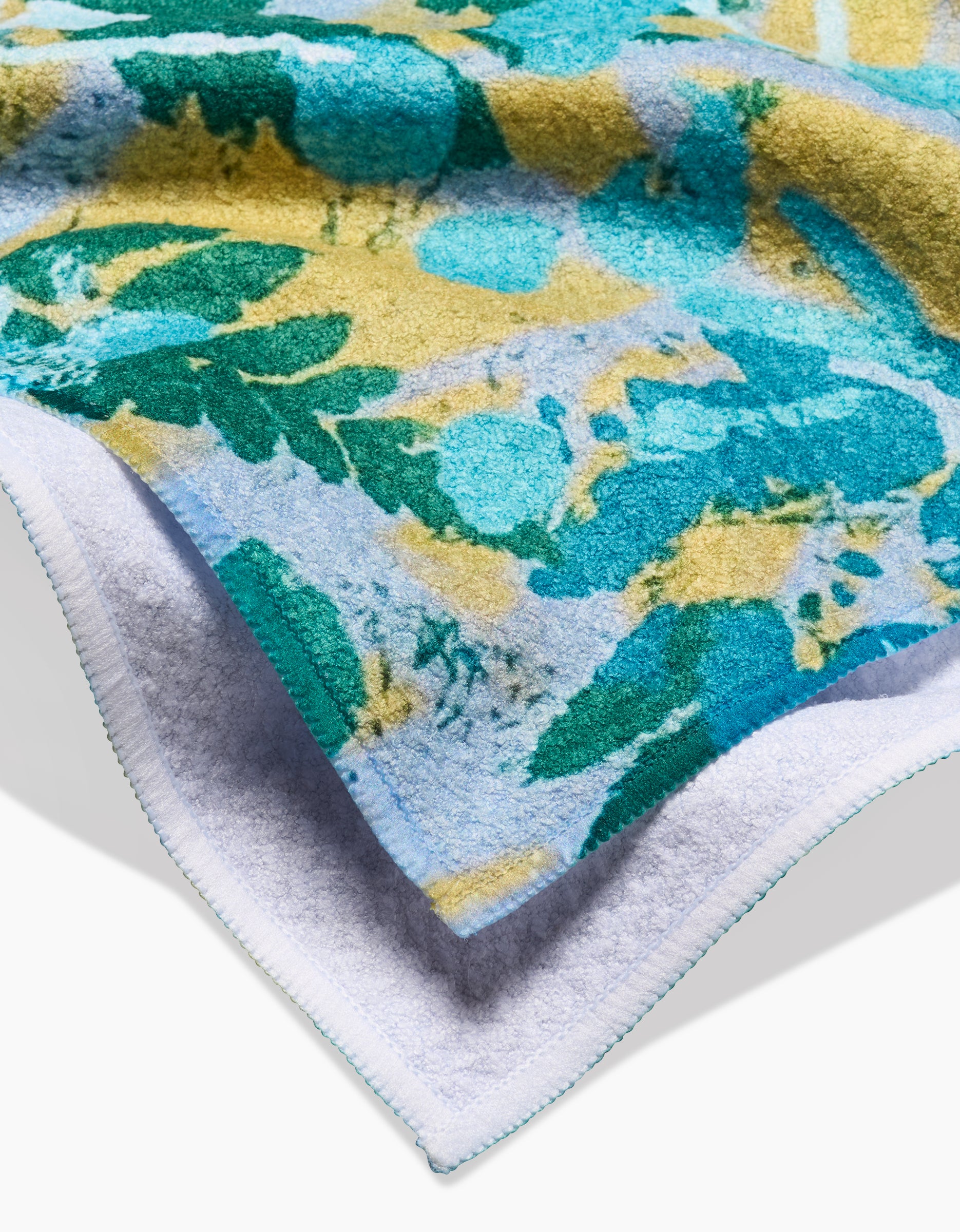 A close-up of the Leafy Bush Tea Towel by Taryn Brennan shows its blue, teal, and yellow abstract floral print, white underside, and blue-stitched border—crafted from recycled materials.