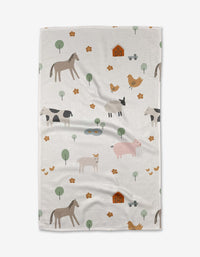 The Coit Creative Light Farm Animals tea towel is crafted from white Geoweave™ fabric and features a playful farm-themed pattern with illustrated animals, barns, trees, and small yellow flowers scattered across the surface.
