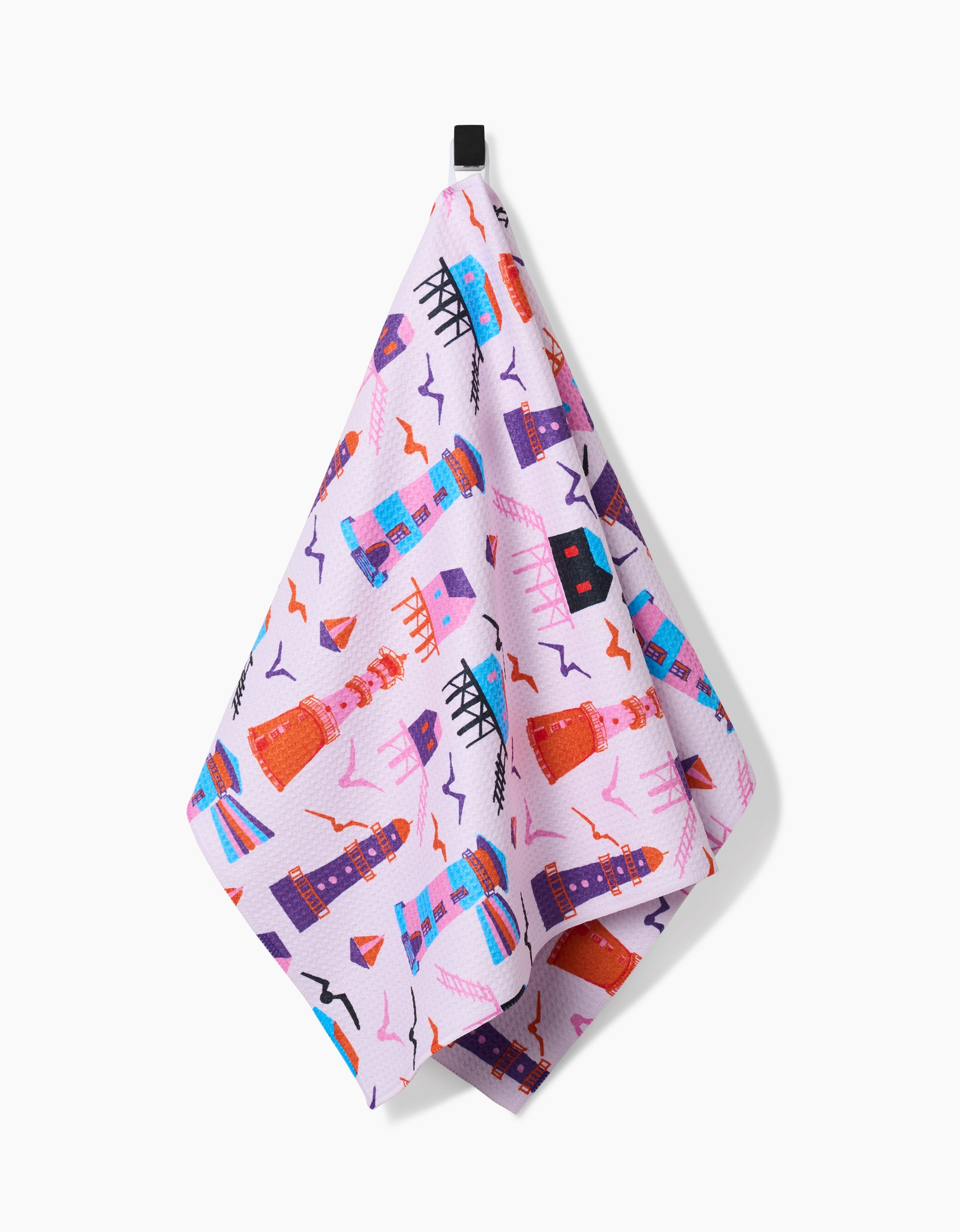 The Lighthouse In Pink tea towel by Ania Zwara Art features a pink geometric design with lighthouses, buildings, and shapes in red, blue, purple, and orange on ultra-absorbent Geoweave fabric with a black hanging loop.