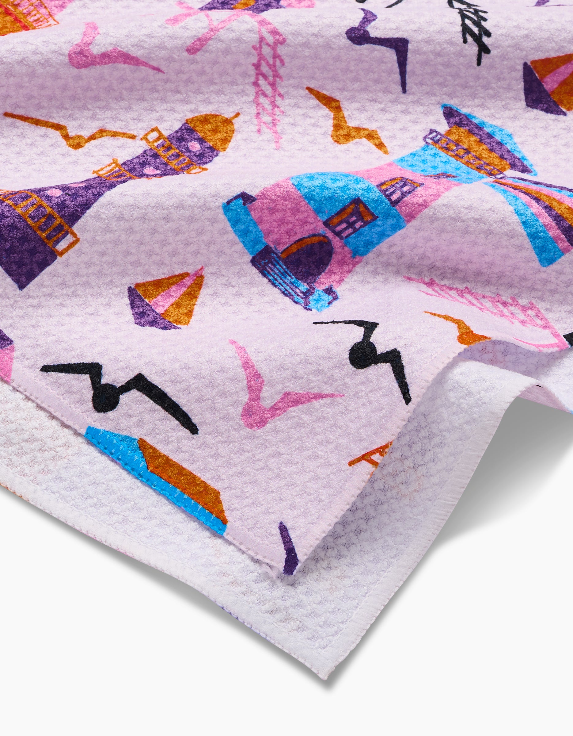 A close-up of the Lighthouse In Pink Geoweave tea towel by Ania Zwara Art shows its ultra-absorbent, textured fabric with vibrant blue, pink, orange, and purple illustrations of lighthouses, sailboats, birds, and houses.