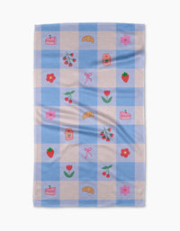 The Little Picnic Things tea towel by Letters By Shells is made from recycled materials and features blue and white checks with embroidered croissants, cherries, strawberries, jam jars, cake slices, pink bows, red tulips, and pink flowers.