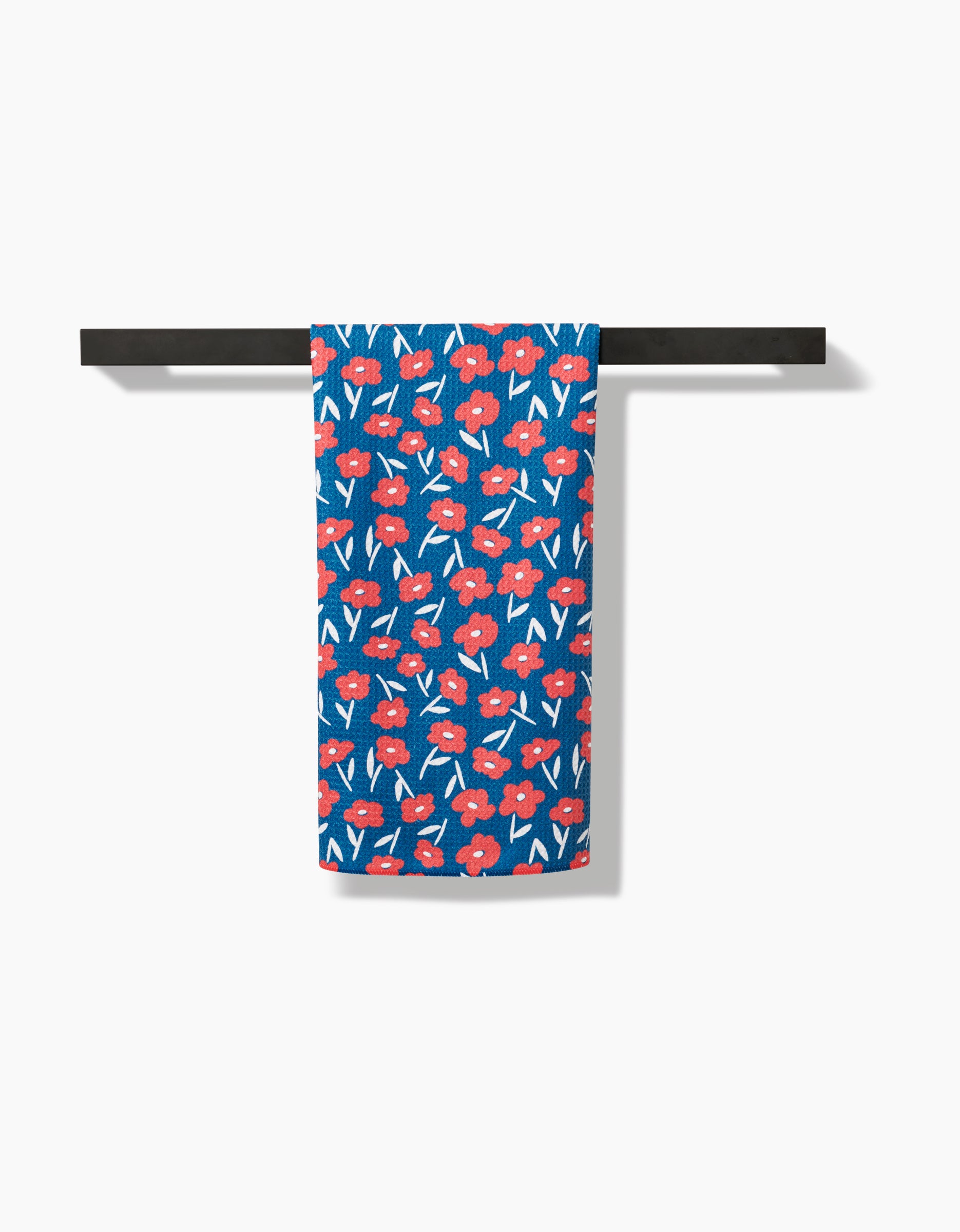 The Luca Daisy Red tea towel by Hufton Studio, featuring a red and white floral pattern, hangs neatly on a black bar against a plain white background.