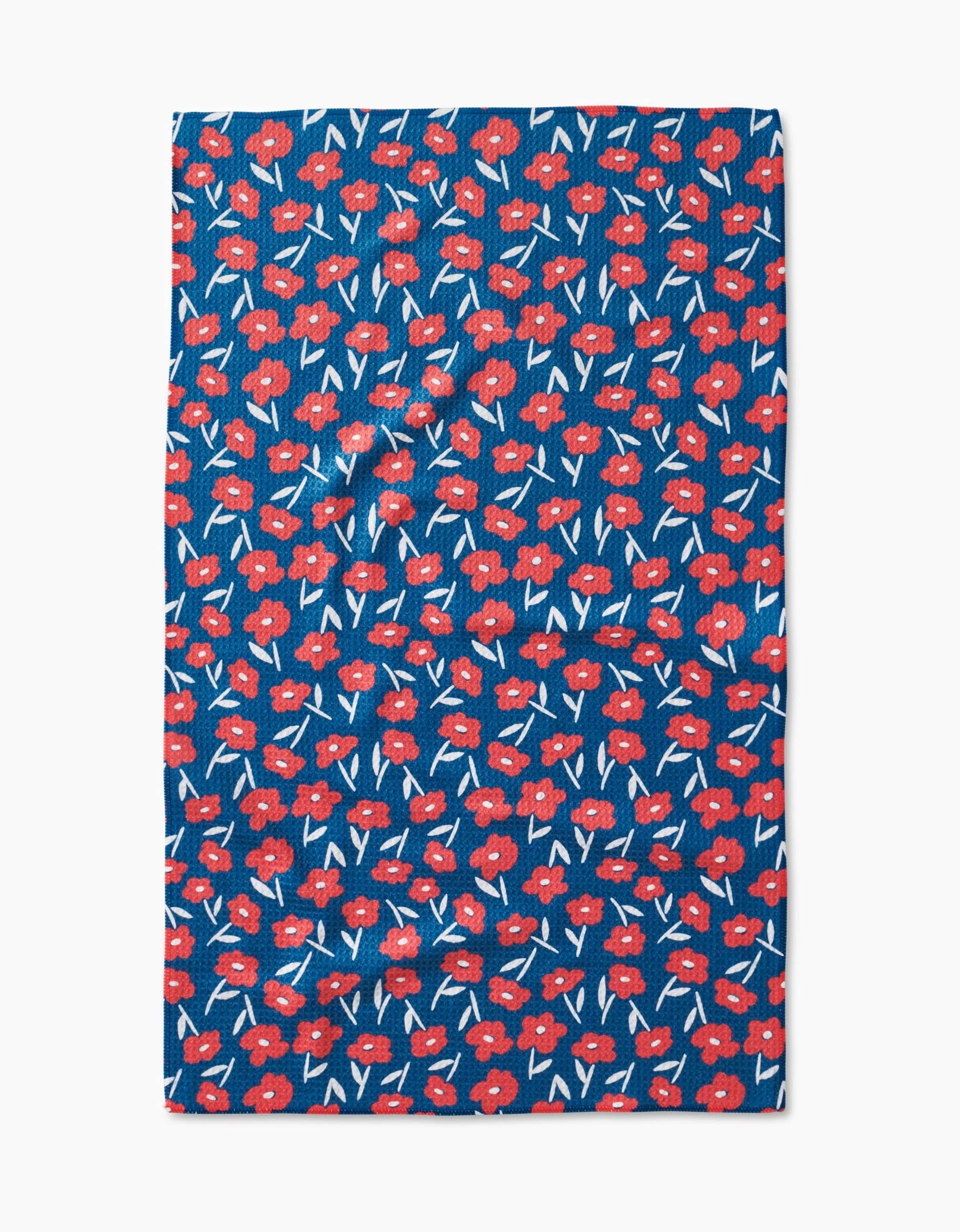 The Luca Daisy Red tea towel by Hufton Studio features a blue background with small red flowers, white accents, and green stems in a repeating pattern, made from recycled materials.