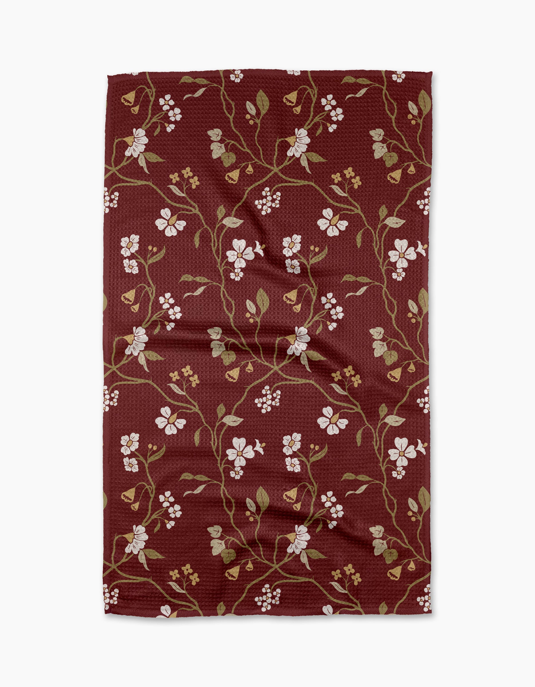 The Lunaria in Merlot tea towel by Danelys Sidron showcases white flowers and green leaves on winding branches over a maroon backdrop. Made from recycled materials, the fabric displays natural folds and creases.