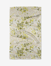 The Lush Garden tea towel from Second Nature Studio features a botanical pattern of green and yellow leaves on thin branches over a light, intricately designed background. Made from recycled materials, it showcases natural wrinkles and soft folds.