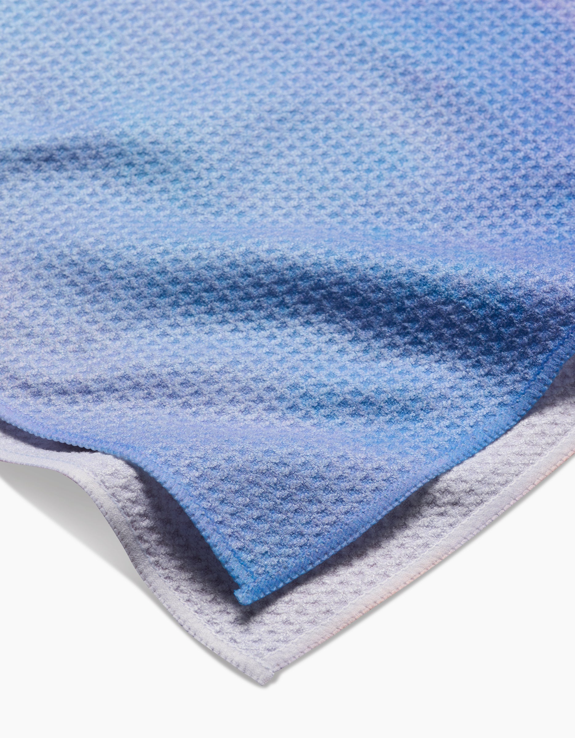 A close-up of the Magic In The Sky tea towel by Stefanie Bales shows its textured Geoweave fabric in blue and light purple gradients—crafted from recycled materials, with one corner slightly folded for detail.
