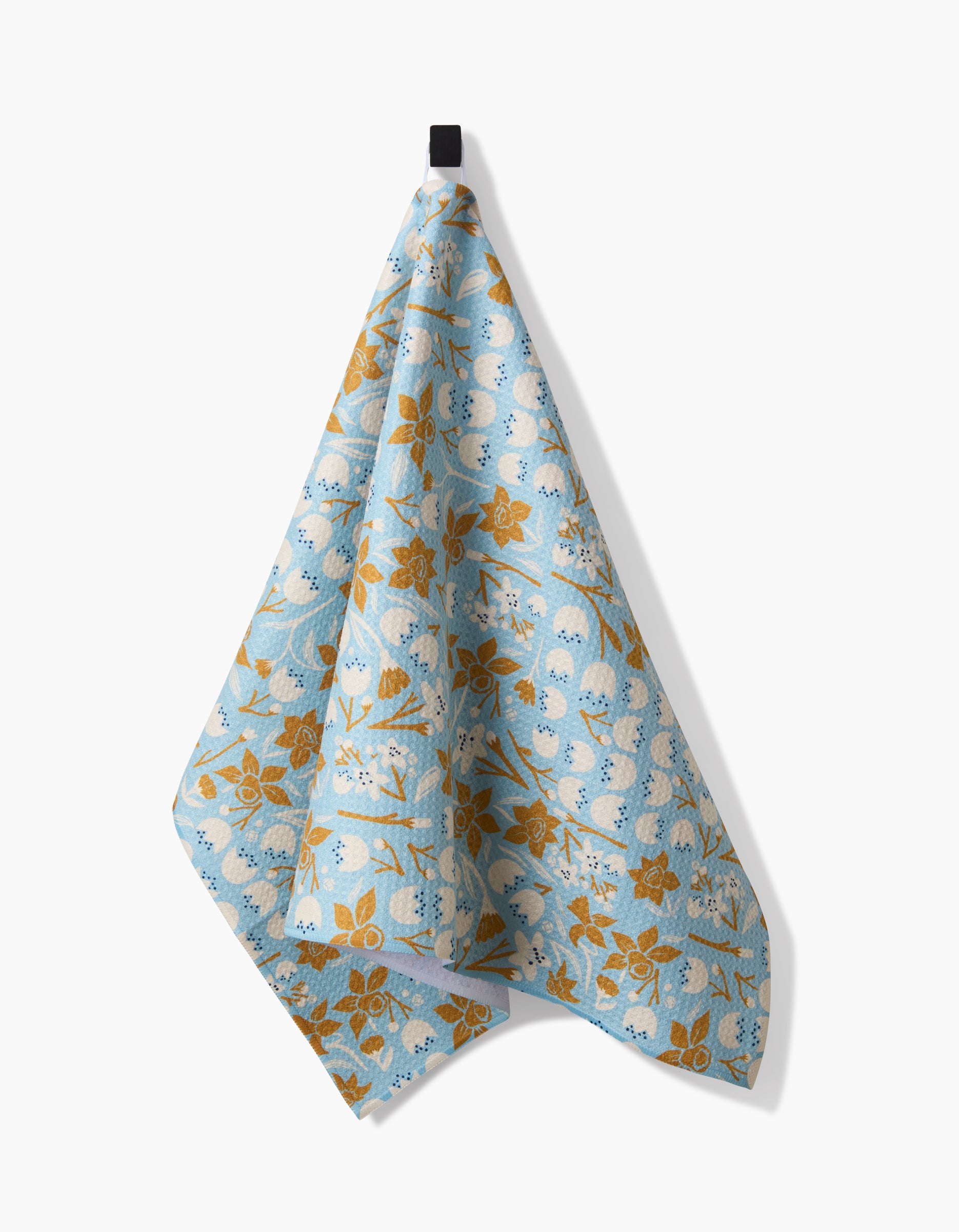 The March tea towel by Elisabeth Wing, made from recycled materials, displays yellow flowers and white circles on light blue fabric and hangs from a black hook against a white background.