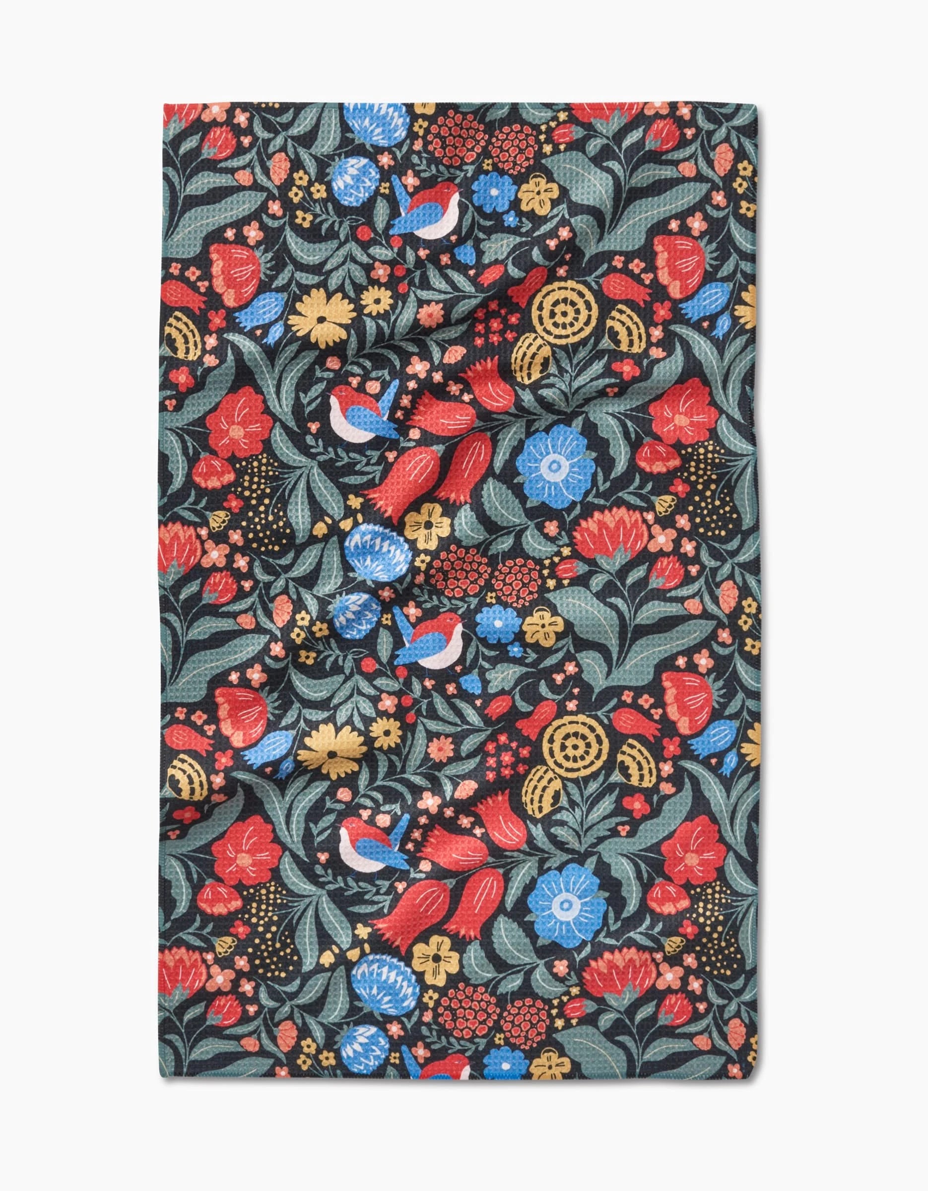 The Marsh Wren tea towel by Danelys Sidron features a vibrant floral and bird pattern with red, blue, and yellow flowers plus green leaves on a dark background, made from ultra-absorbent Geoweave fabric in a rectangular shape.