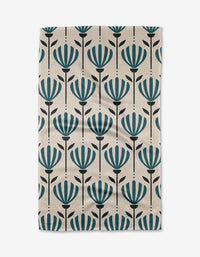 The Martine tea towel by Amy MacCready is a rectangular beige design made from recycled materials, featuring vertical rows of stylized teal flowers with black stems and leaves.