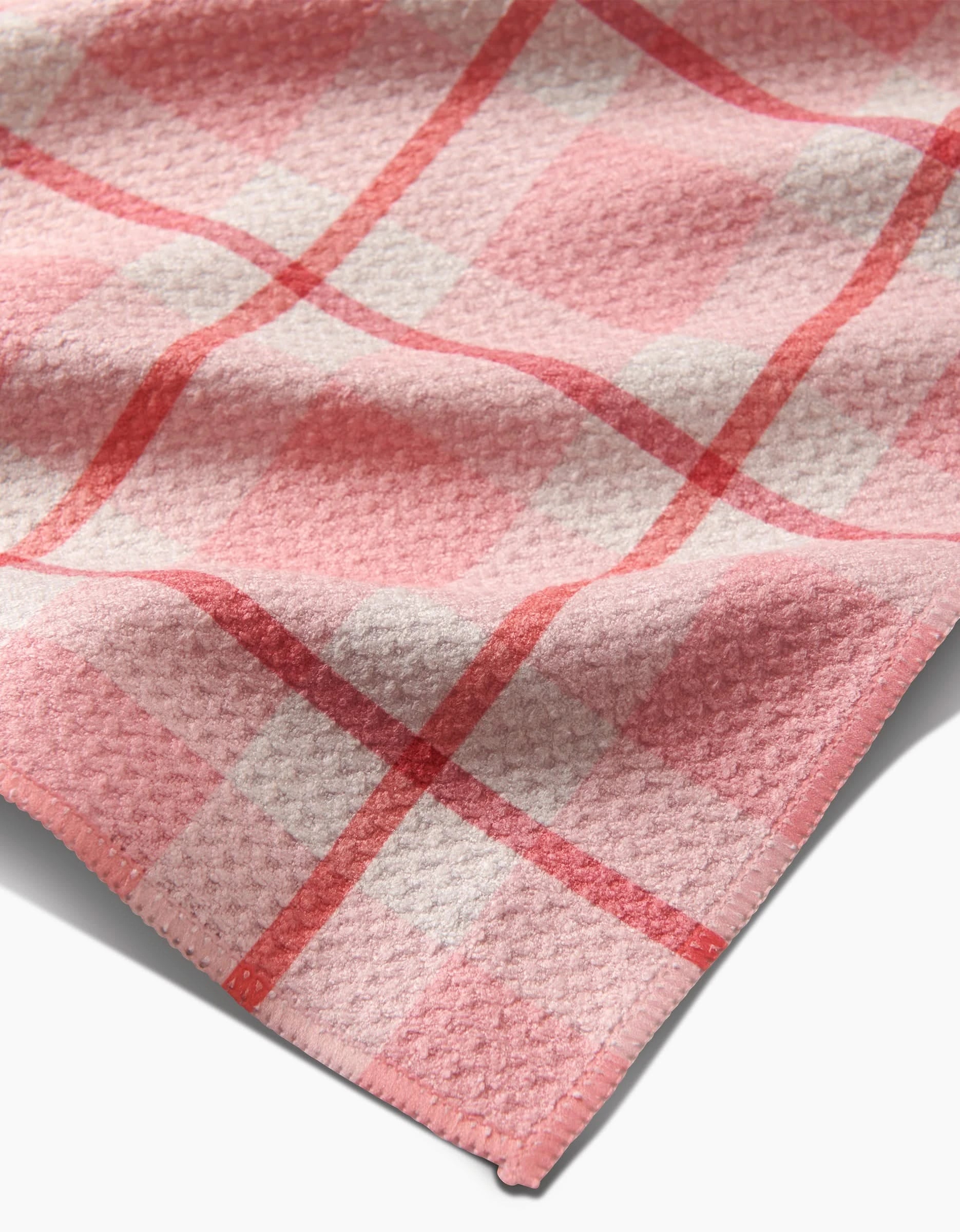 A close-up of the Marva Lu tea towel by Kelsi Fullmer, featuring a pink, red, and white checkered pattern on recycled fabric with stitched edges. The textured material is slightly wrinkled.