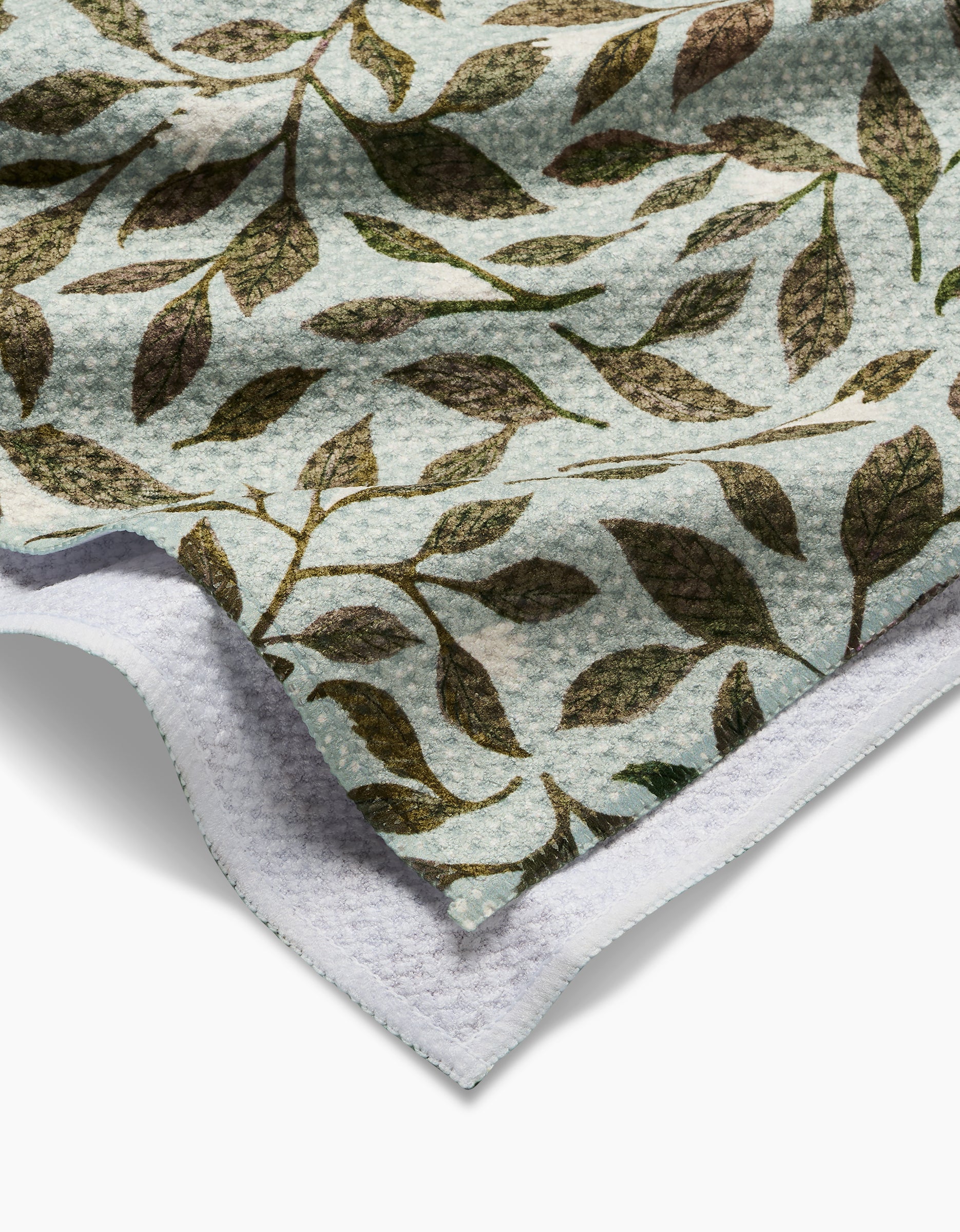 Close-up of Katie OSheas Mint Leaves tea towel, showcasing a leafy branch pattern in green and brown on a light background with a white underside. Crafted from durable, absorbent Geoweave Fabric.