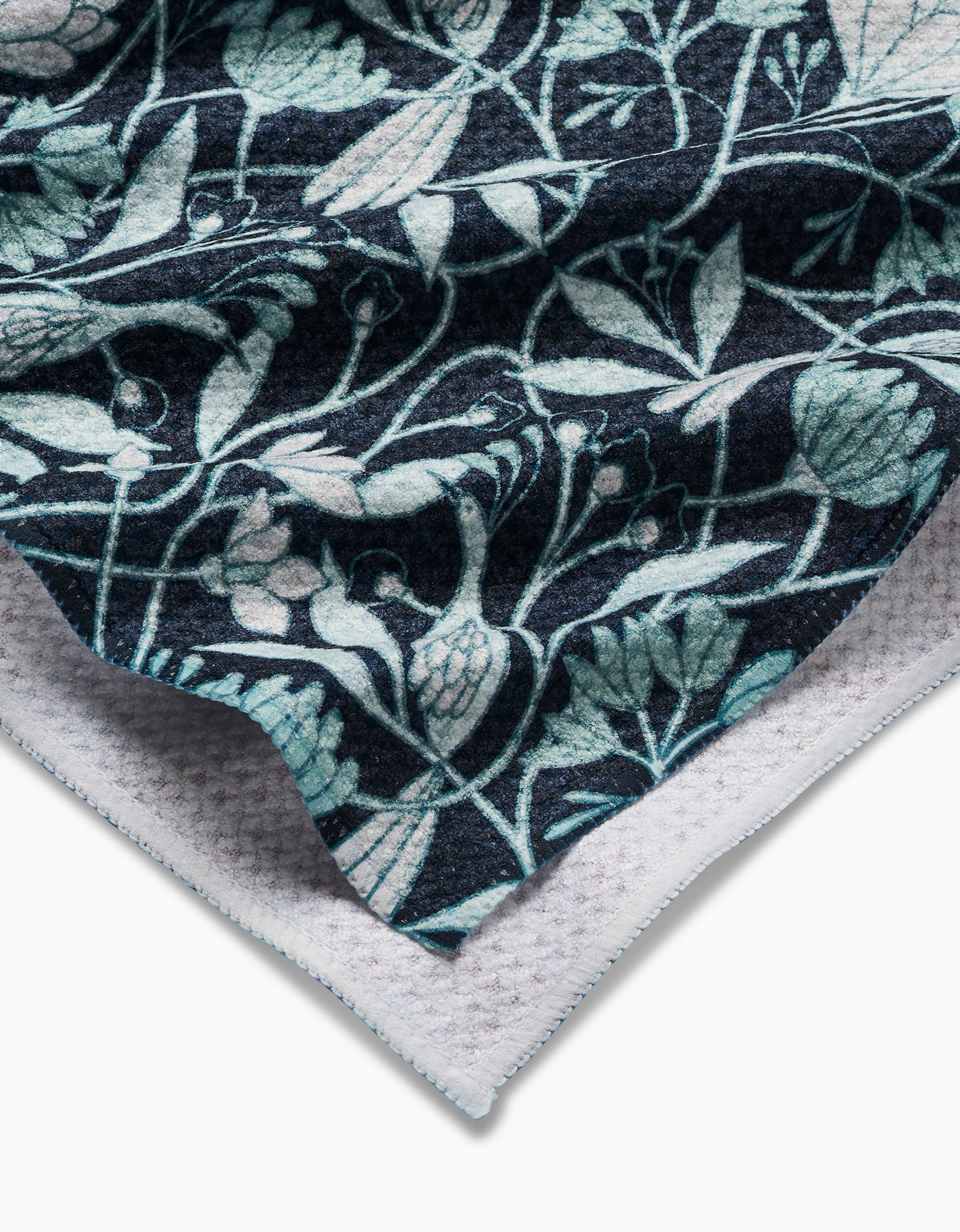 A close-up of the Mirielle by Amy MacCready shows folded Geoweave fabric with intricate blue and green floral and leaf motifs on a dark background, highlighting its textured white underside.