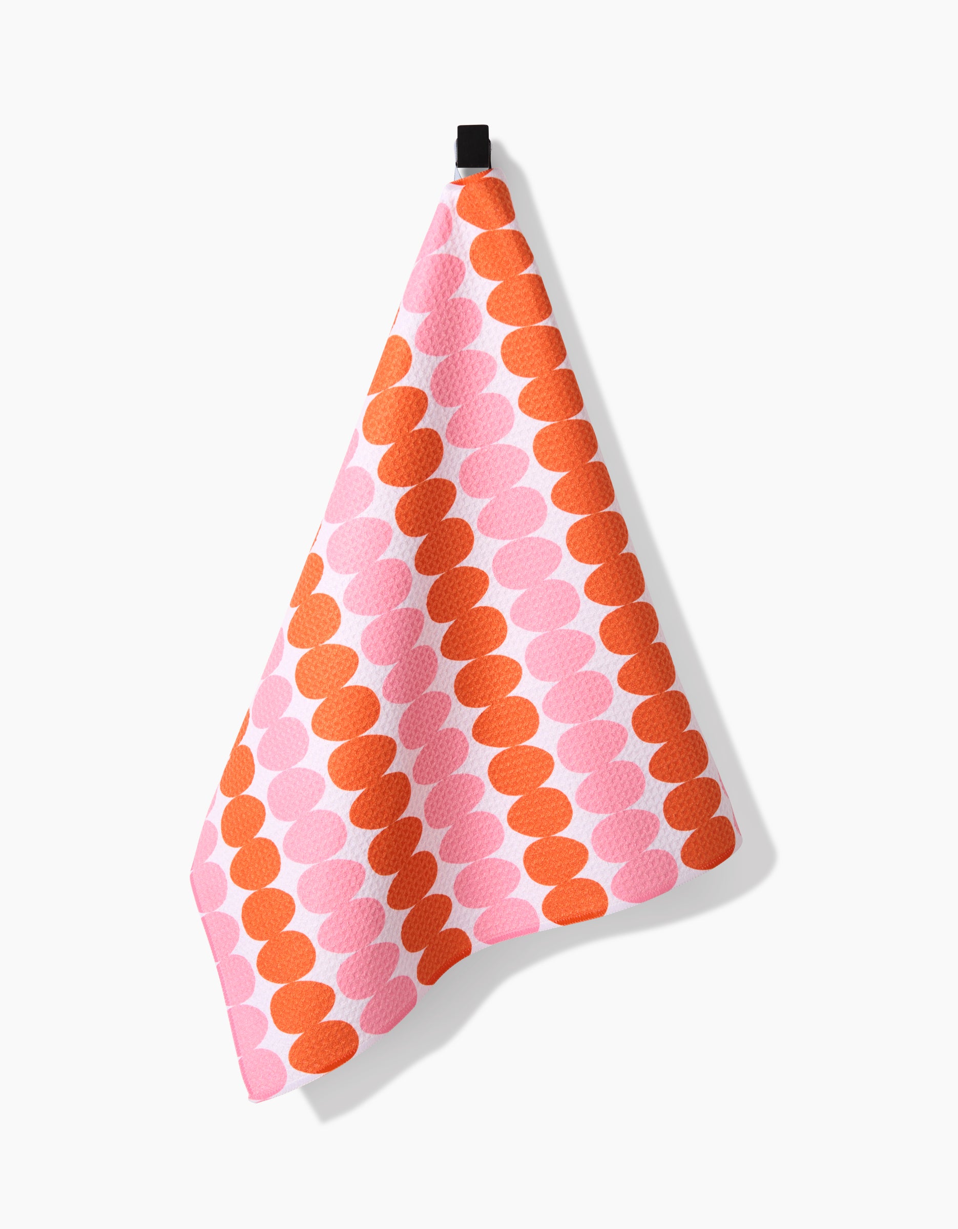 The Kayla Ann Modd Egg Tea Towel, made from recycled materials and featuring orange and pink ovals in diagonal rows, hangs by a black loop against a white background.
