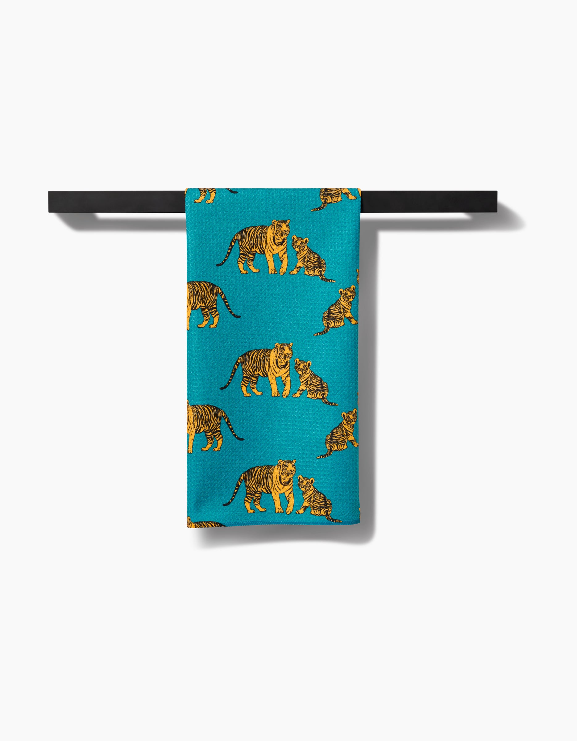 The Mommy and Me tea towel by Sarah Holden features yellow and orange tigers with cubs on blue Geoweave fabric, shown hanging on a black bar against a white background.