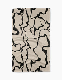 The Monochrome Liquid tea towel by Marina Solodka is beige, rectangular, made from recycled materials, and features an abstract black squiggly line pattern—shown laid flat on a white background.