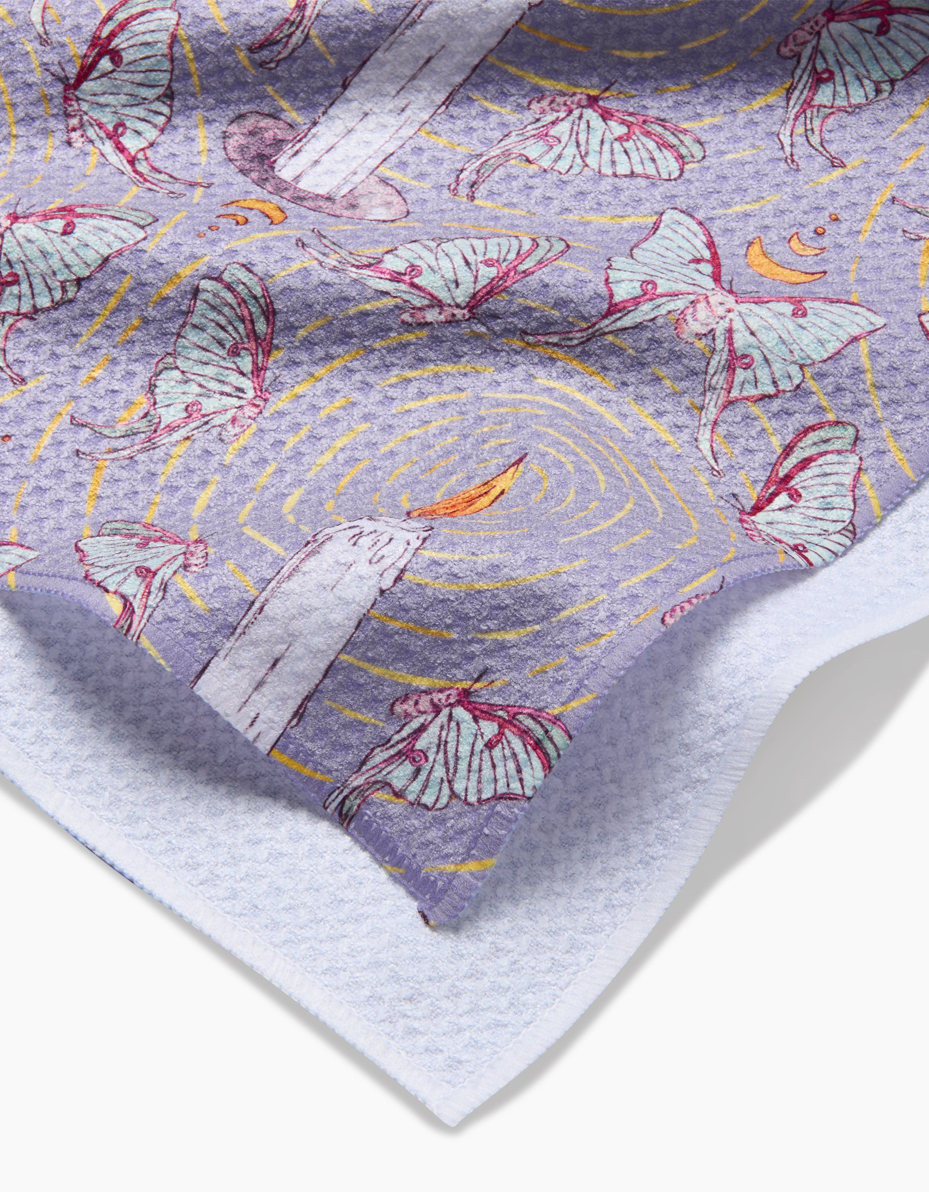 A close-up of Maayan Alper-Swans Moth To A Flame Geoweave tea towel shows white moths circling candles, swirling yellow lines, and crescent moons on a purple background, finished with a soft, waffle-like edge for unique texture.