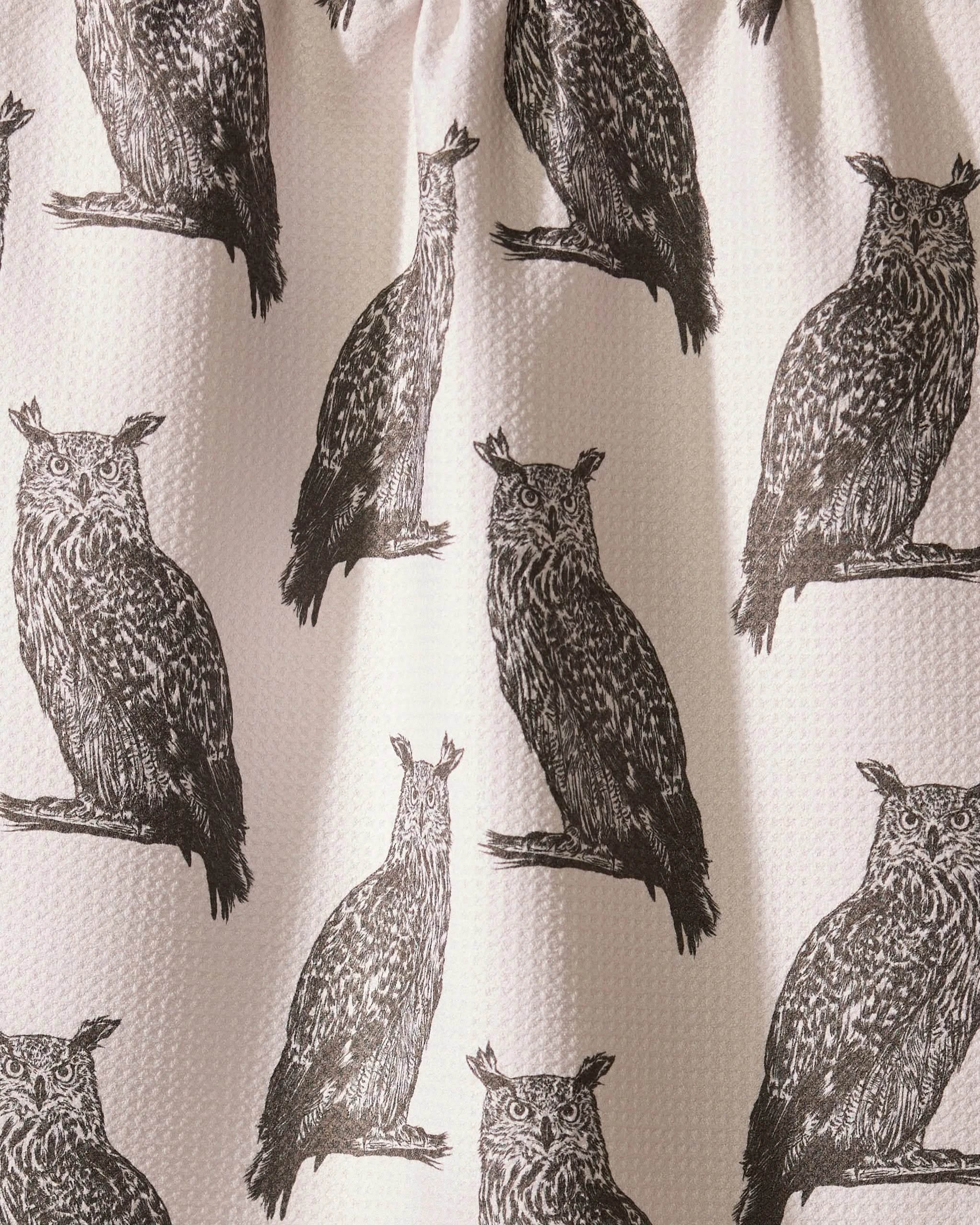 The Geometry Nocturne recycled kitchen towel showcases repeated black owl prints on a light, textured background. A center owl is uniquely distorted by a fabric fold.