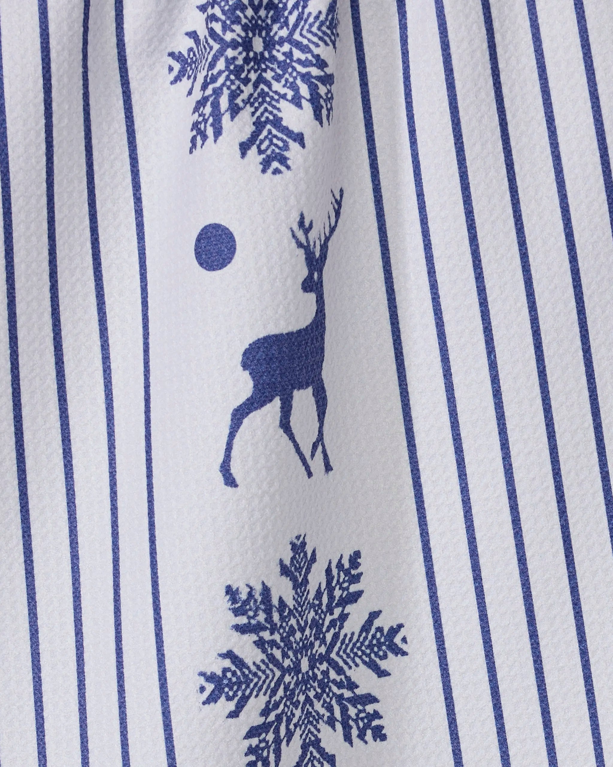 The Geometry Nordic Stag kitchen towel is white with vertical blue stripes and blue prints of snowflakes, a reindeer, and a circle. Made from recycled materials, the fabric has a slightly textured look.