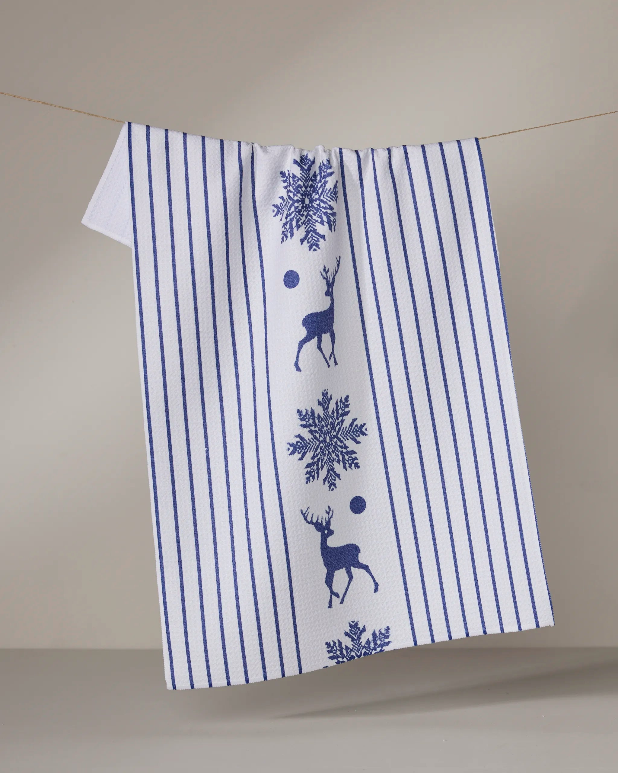 The Geometry Nordic Stag kitchen towel, made from recycled materials, features blue vertical stripes and reindeer on white. It’s shown hanging against a light gray background—an eco-friendly choice with stylish Nordic design.