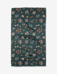 The North Meadow tea towel by Charlie Rowan Designs features a dark green Geoweave™ fabric with colorful strawberries, cherries, bees, flowers, leaves, and small geometric shapes scattered across the surface.