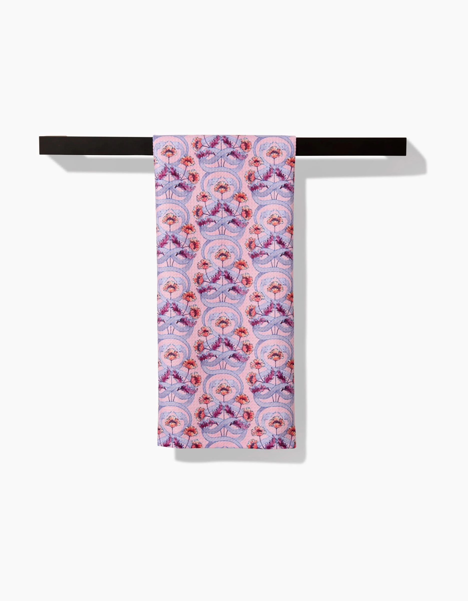 The Maayan Alper-Swan Nouveau Snake towel, featuring pink and purple patterns in floral and fan motifs on ultra-absorbent Geoweave fabric, is neatly draped over a black towel bar against a white background.