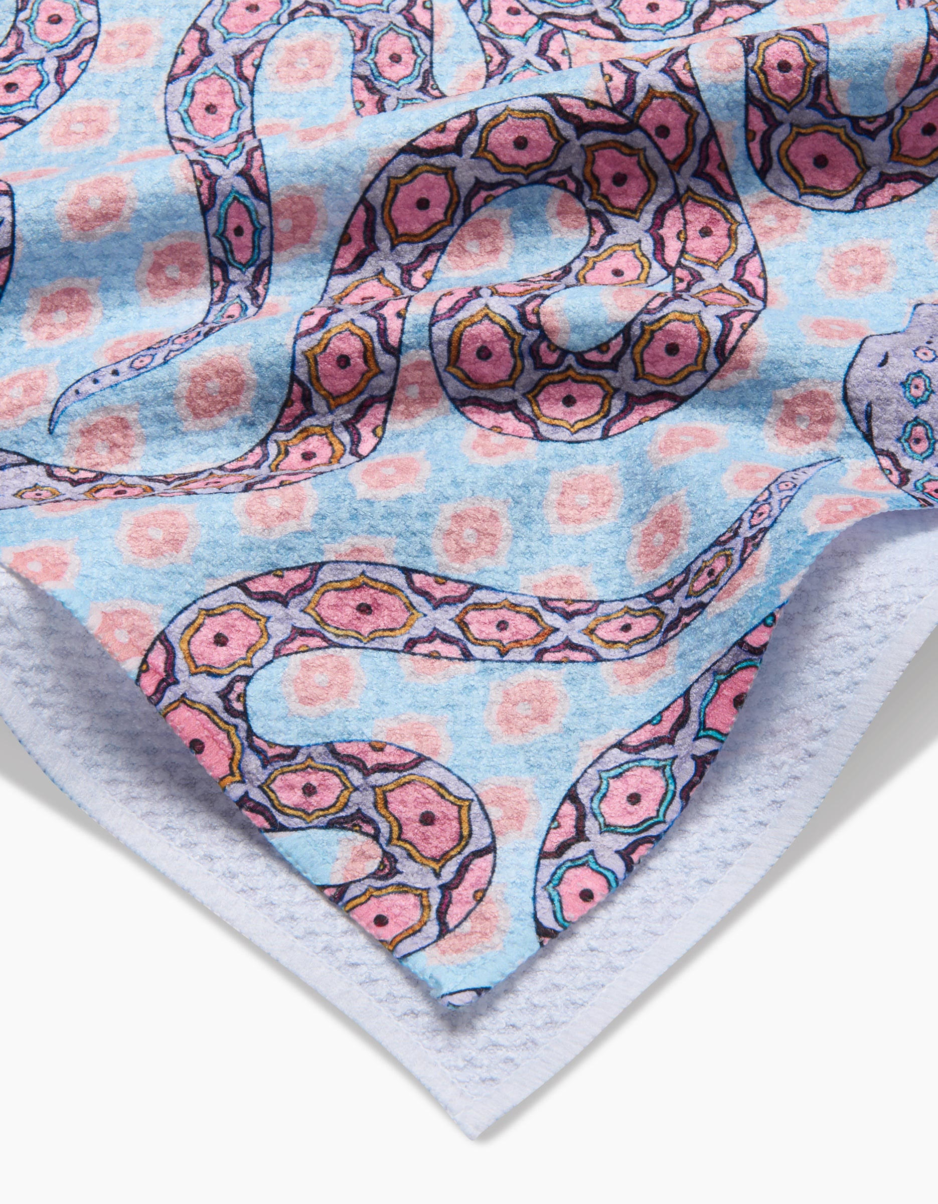 A close-up of the Ophidia tea towel by Maayan Alper-Swan, showing its soft, blue fabric with a vibrant pink and purple snake pattern, geometric motifs, and floral shapes. Made from ultra-absorbent post-consumer recycled materials.