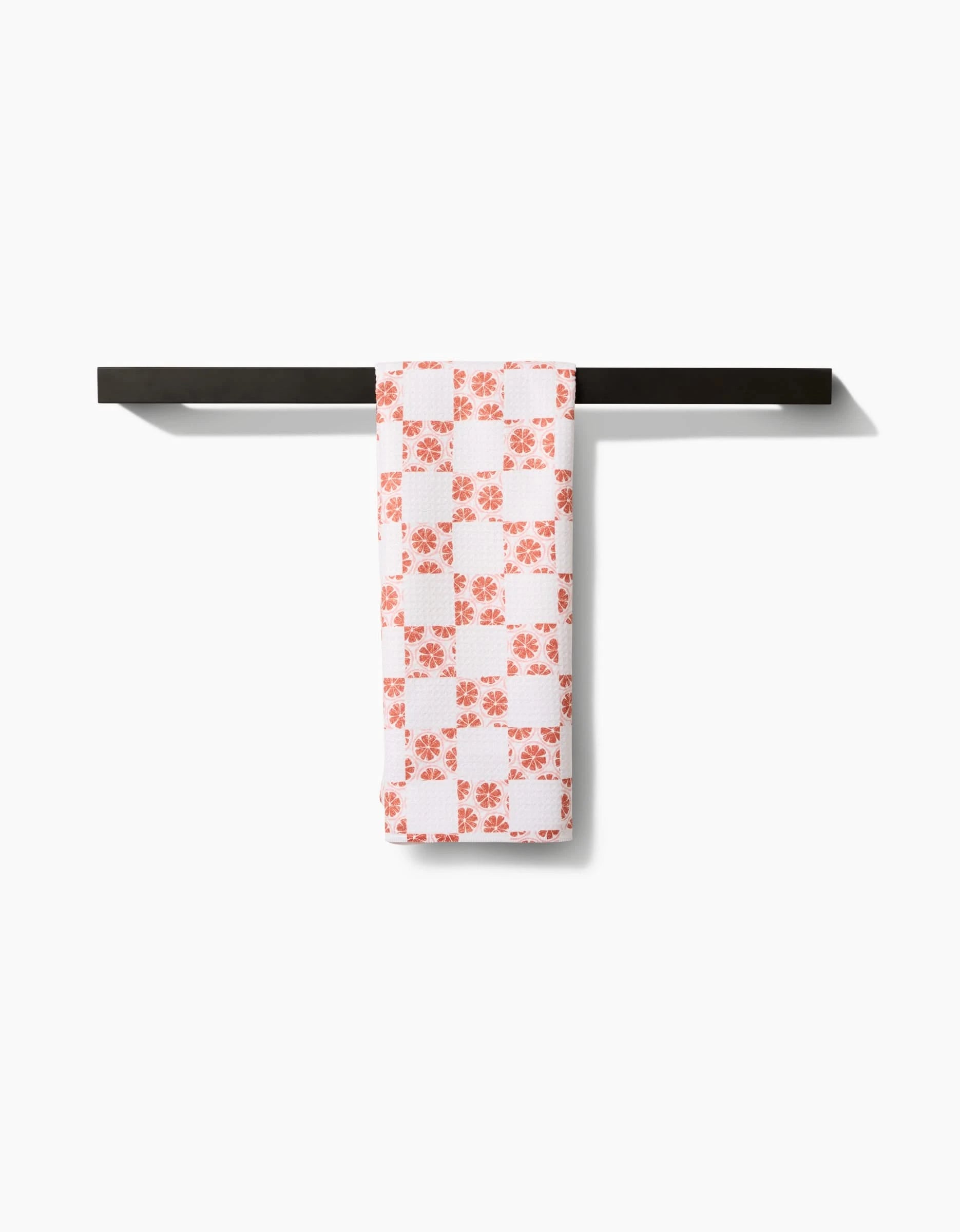An Orange Checker tea towel by Teri the Butter, featuring a bold checker pattern on Geoweave™ fabric, hangs neatly on a simple black towel bar against a plain white background.