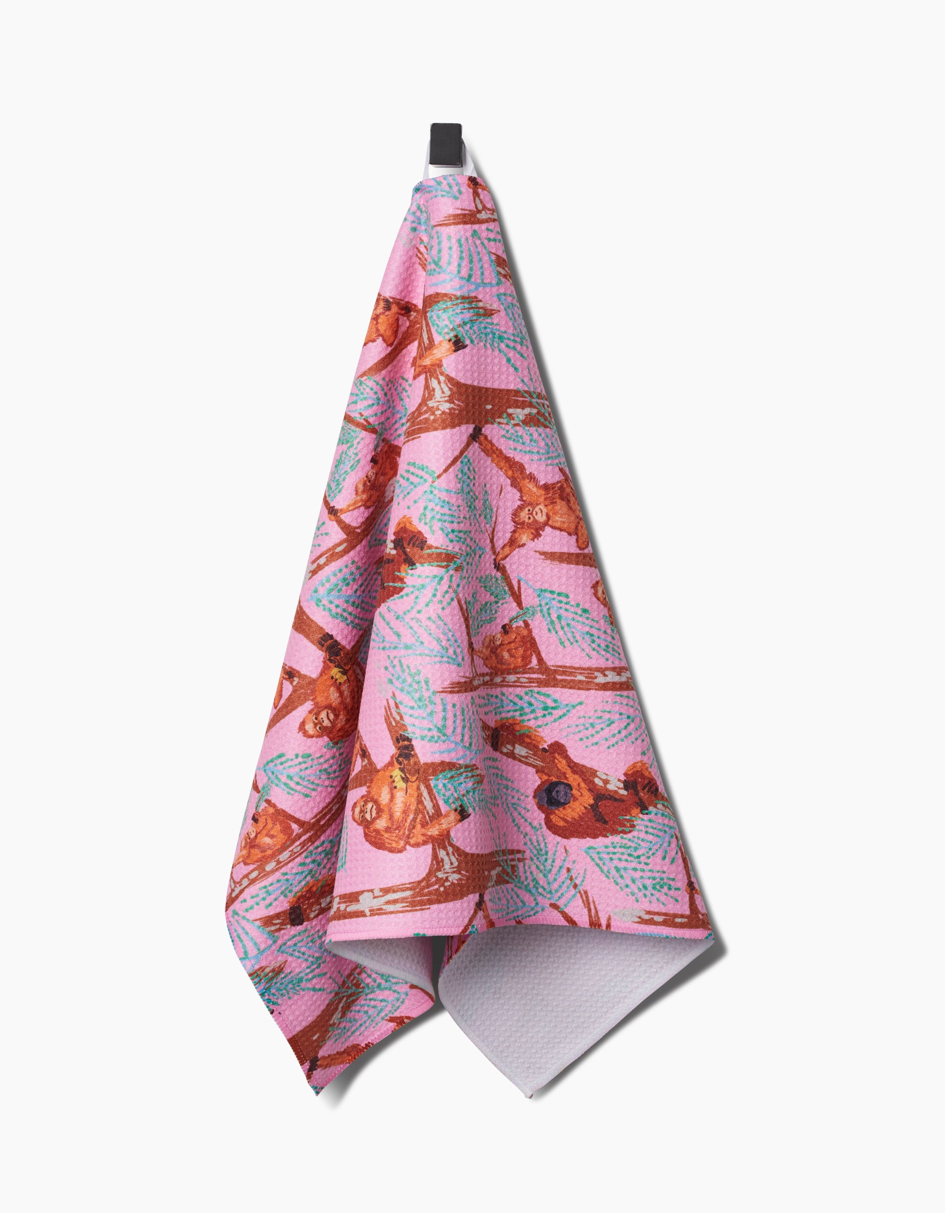 The Orangutan Clan tea towel by Elisabeth Wing, made from recycled materials, features a colorful design of brown orangutans and green palm leaves and hangs against a white background.